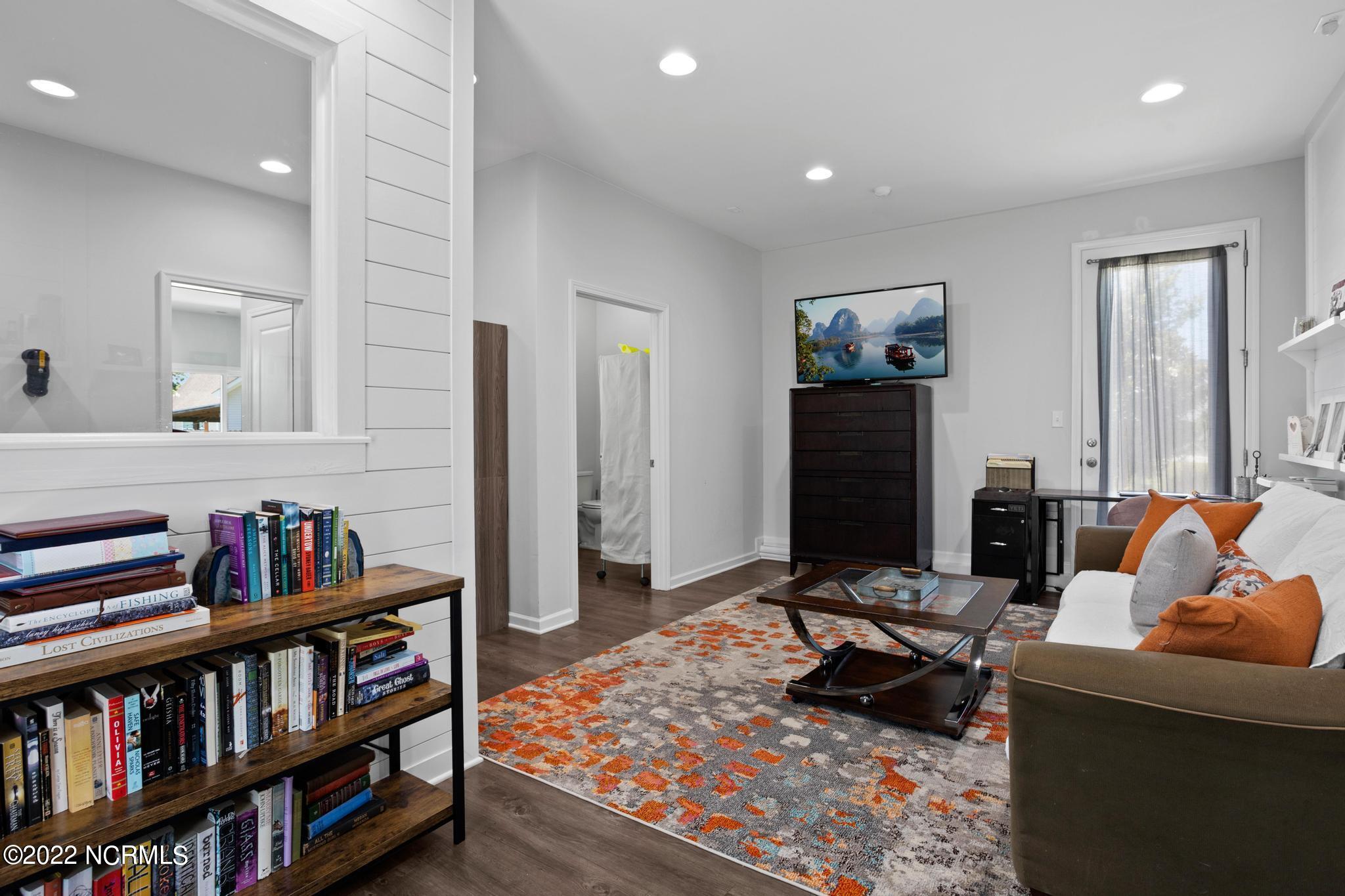 Furnished living room with orange-accented rug, white sofa, and book-filled shelves.