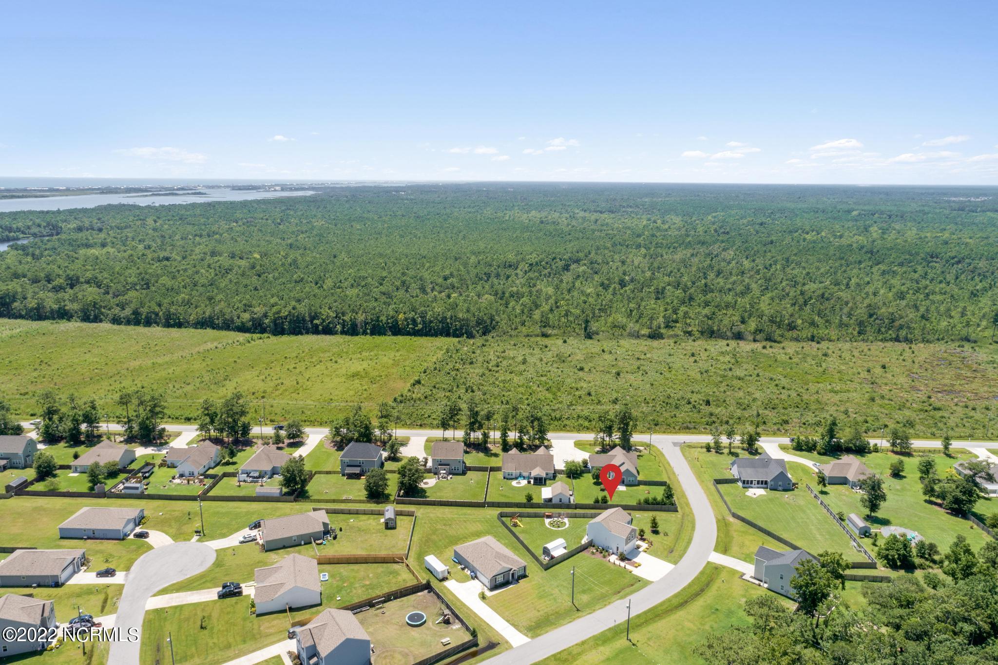 Aerial view of a neighborhood home marked beside expansive forest, with distant water.