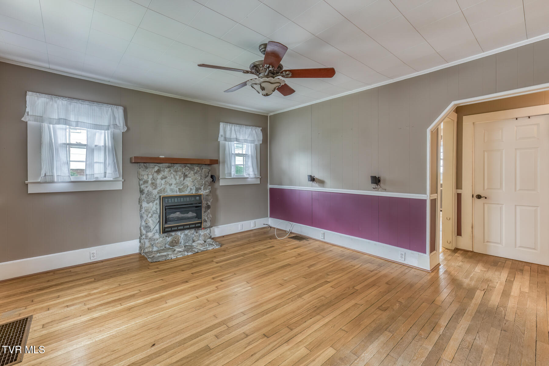 Living room with a stone fireplace, hardwood floors, and a ceiling fan.
