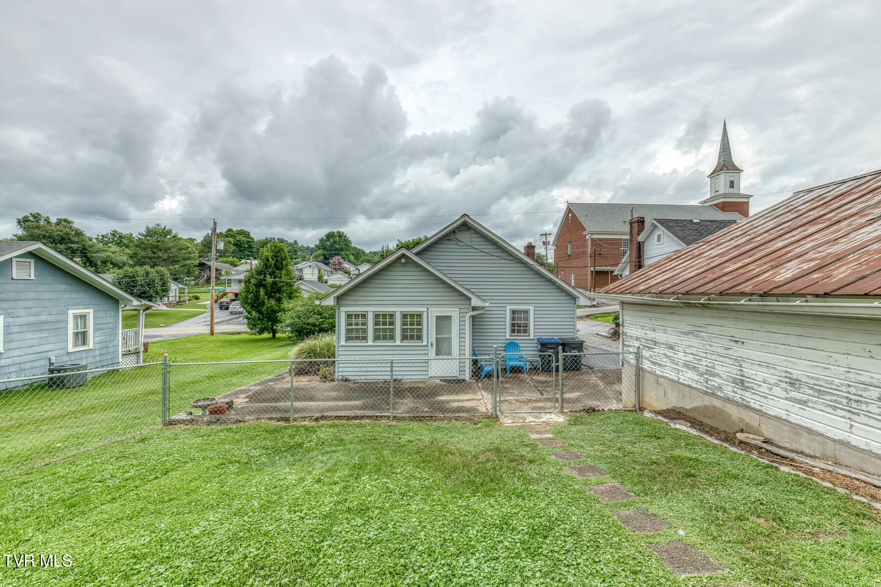 Backyard of 320 Virgil Avenue with a fenced lawn, concrete patio, and blue-sided house.