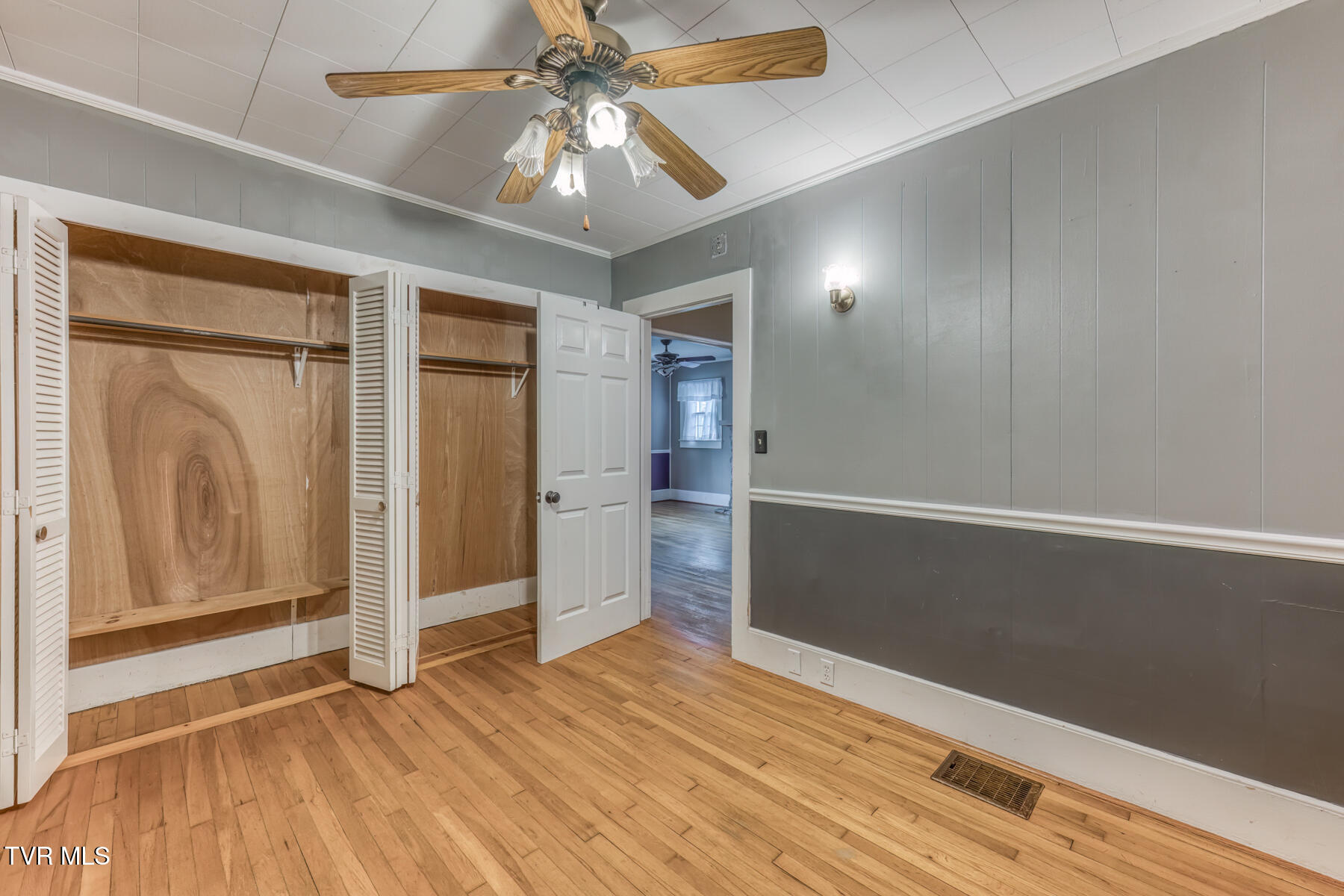 Empty bedroom with open closets, hardwood floors, and a ceiling fan.