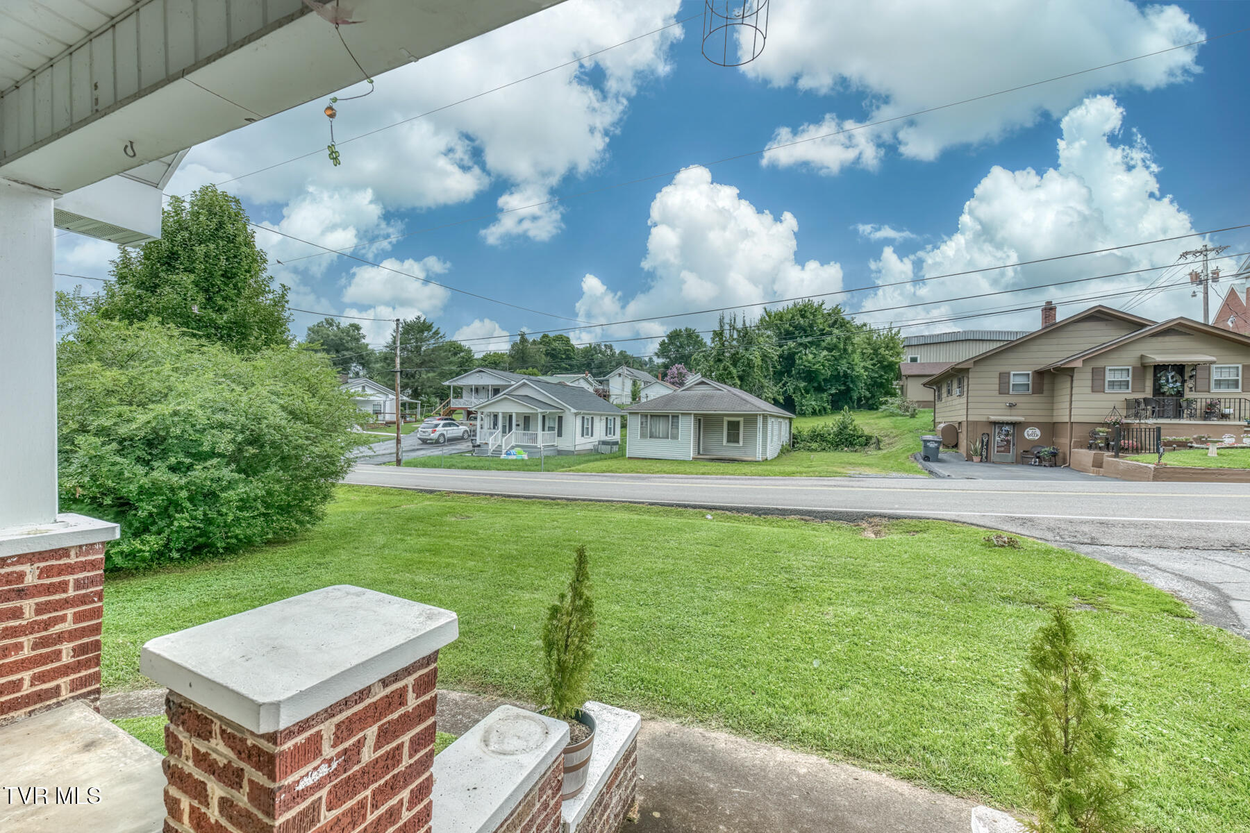View from a covered porch across a lawn and street toward neighboring homes.