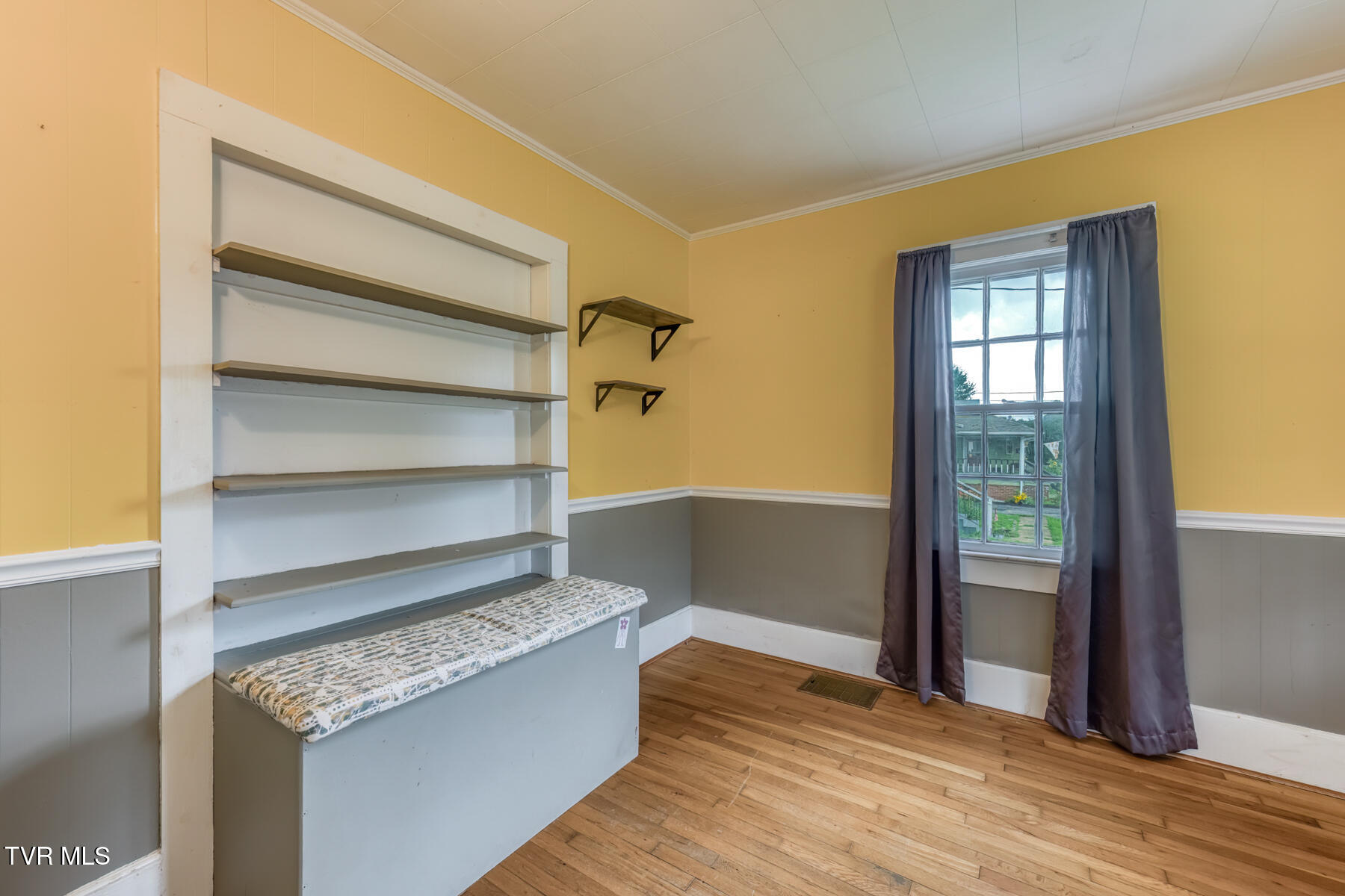 Room with built-in shelves, a padded counter, and a curtained window.