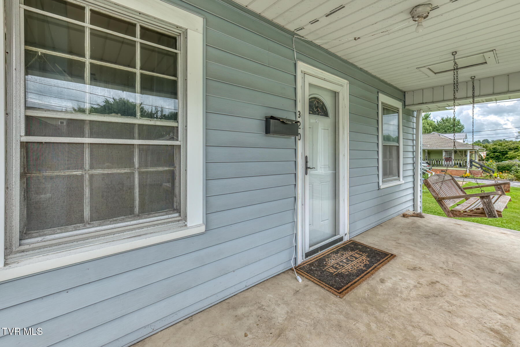 Covered front porch with blue siding, white entry door, screened windows, and a hanging wooden swing.