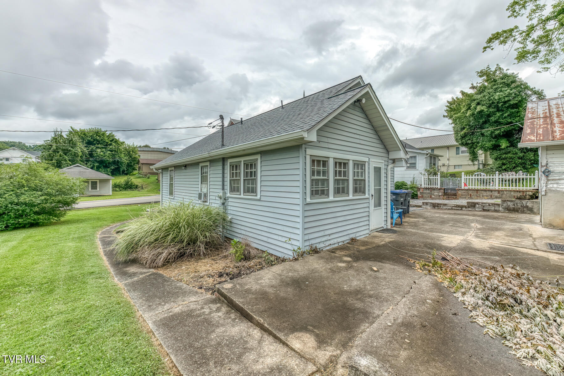 Gray-sided house with a steep gabled roof, lawn, and broad concrete driveway.