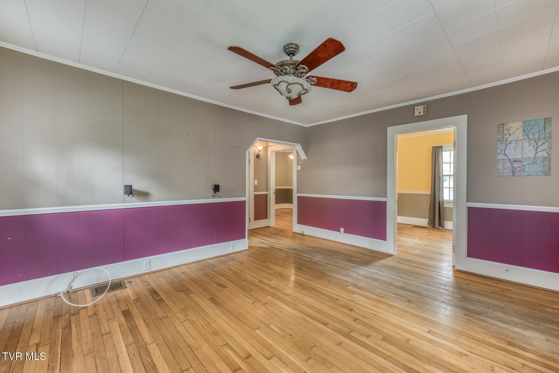 Empty room with hardwood floors, burgundy wainscoting, and a ceiling fan.