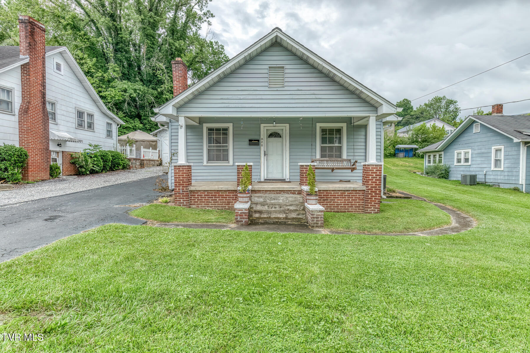 Light blue house with a covered porch, brick steps, and a hanging bench.