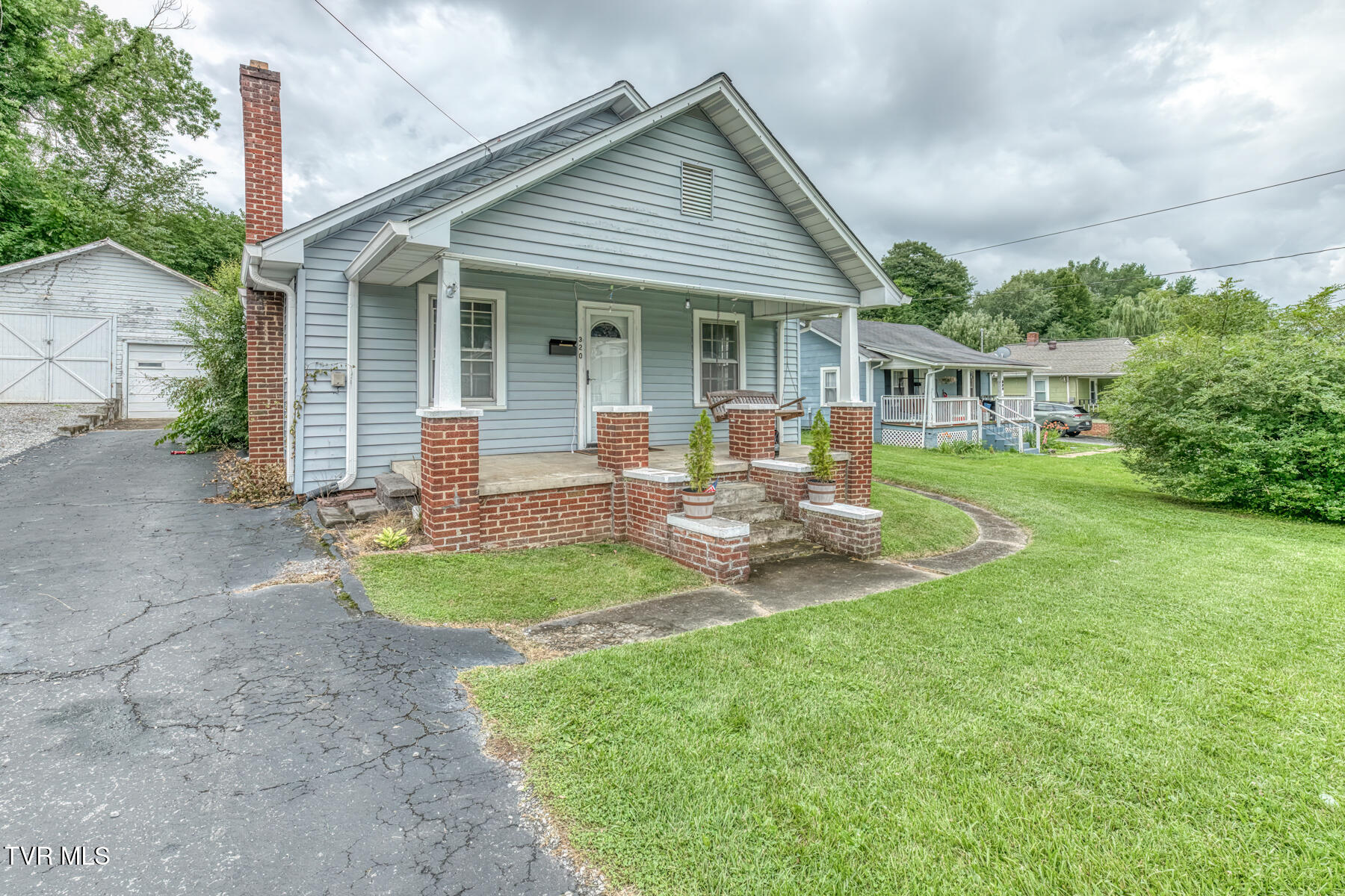 Light blue house with a brick-column front porch, driveway, and detached garage.