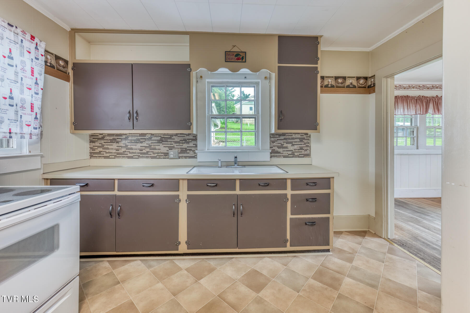 Kitchen with taupe cabinets, a tiled backsplash, and a sink beneath the window.