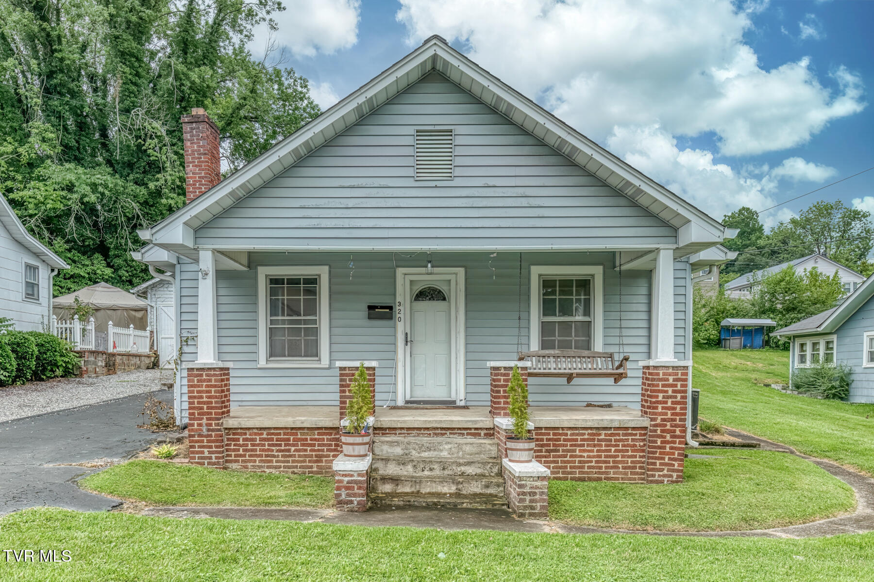 Blue-sided house with a brick porch, white front door, and hanging porch swing.