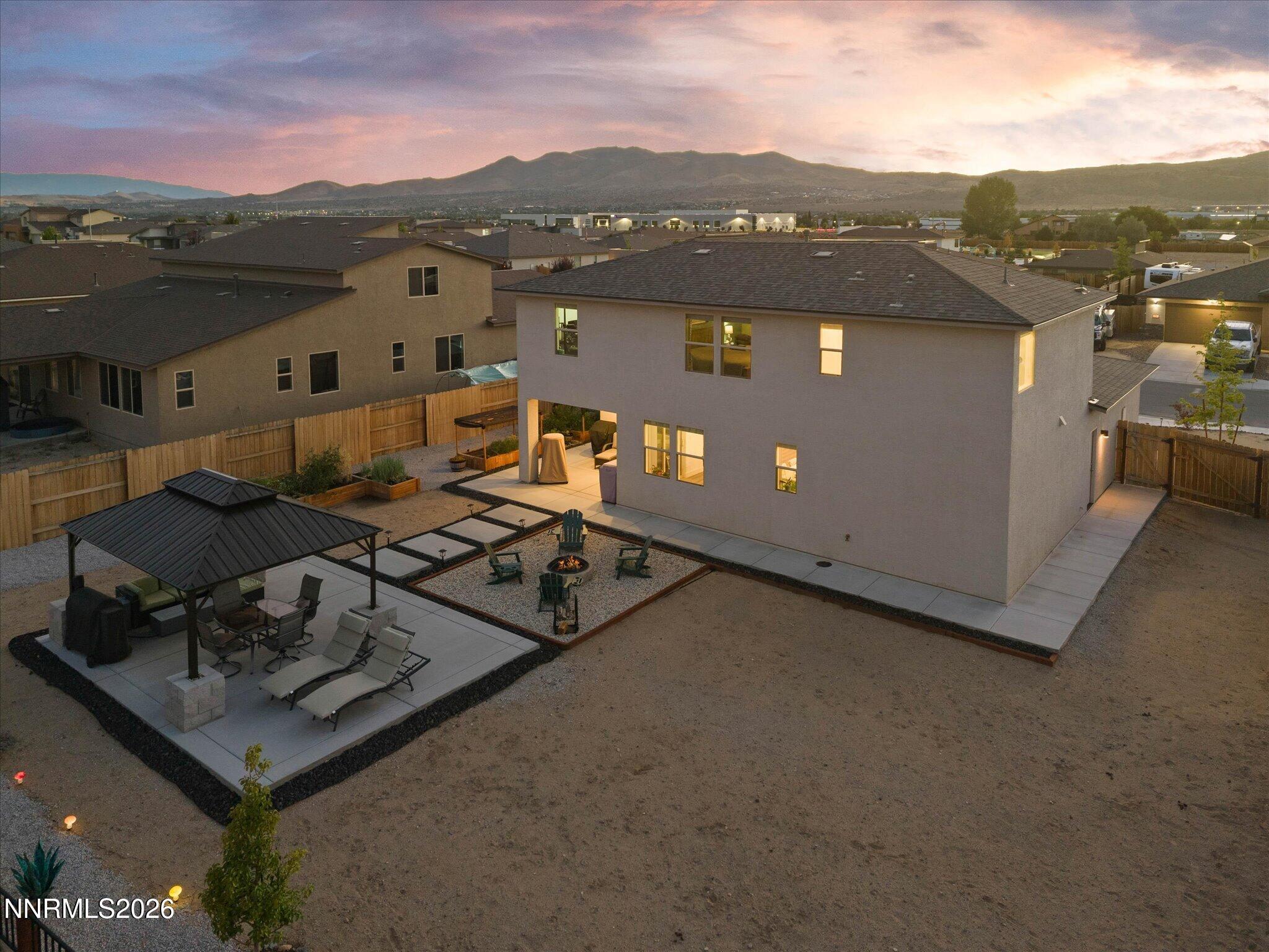 Two-story home and backyard patio with a pergola, fire pit, and distant mountain views at dusk.