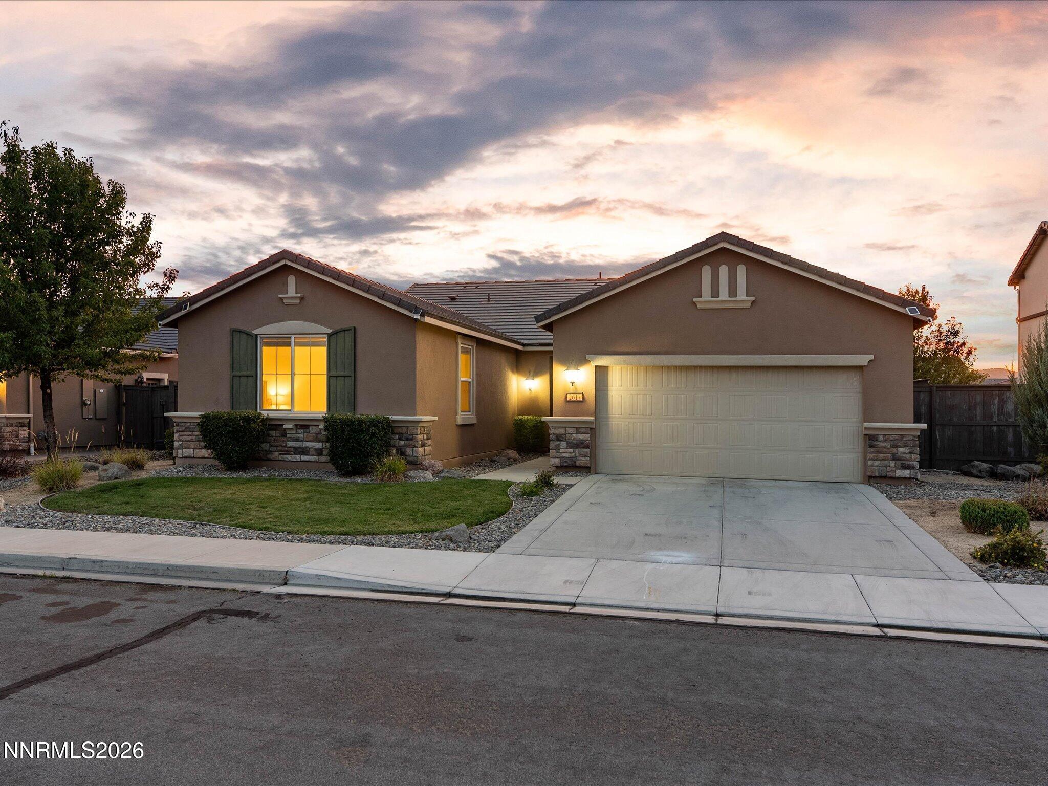 Single-story stucco home with a two-car garage and warmly lit windows at dusk.