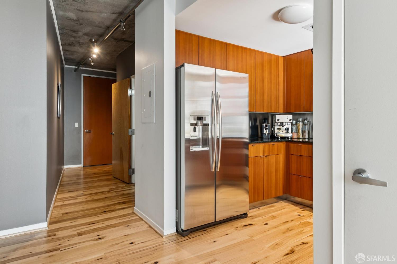 Kitchen with warm wood cabinets, stainless steel refrigerator, and hardwood floors beside the entry hallway.
