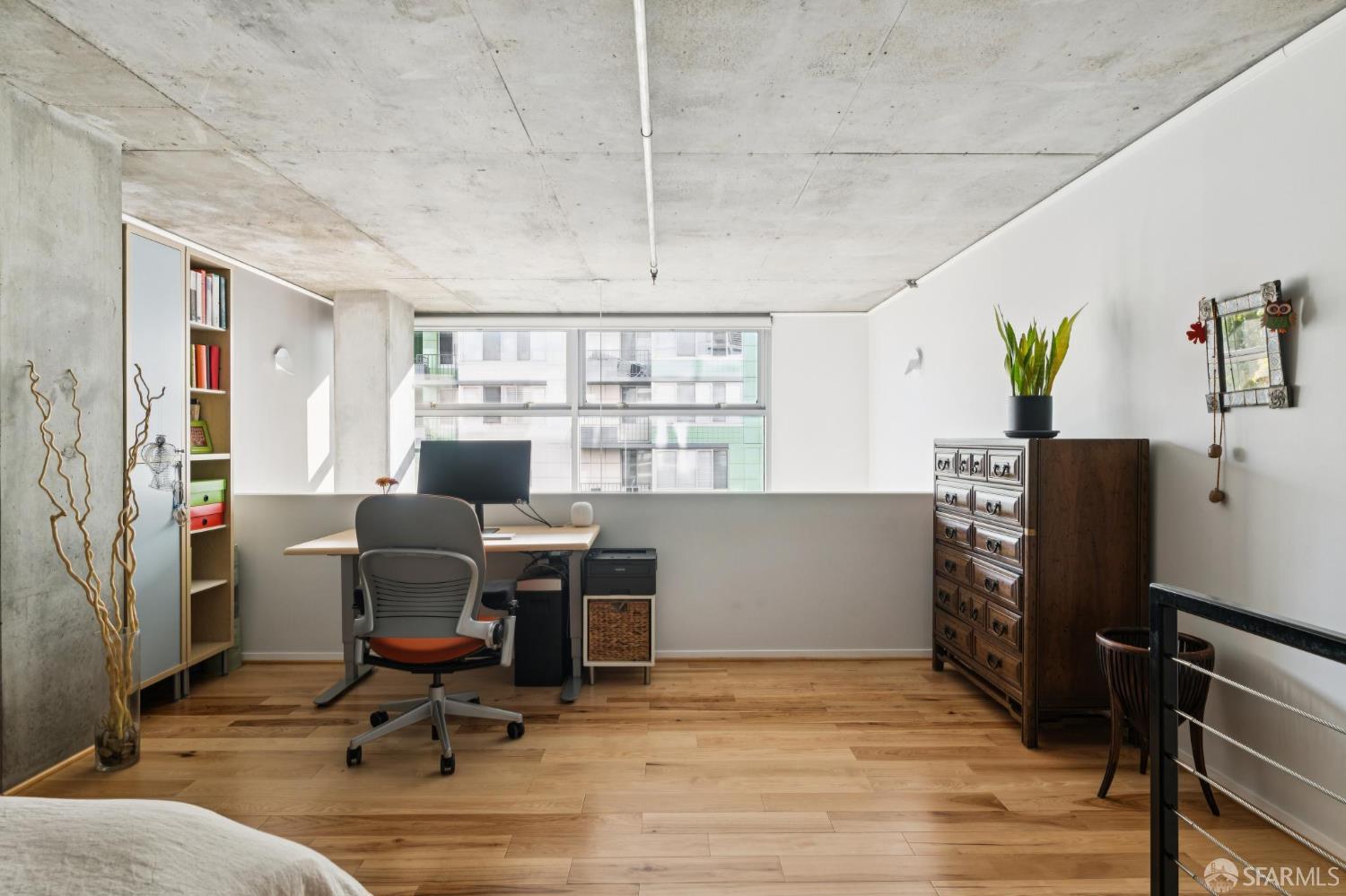 Bedroom workspace with a desk, large windows, hardwood floors, and exposed concrete ceiling.