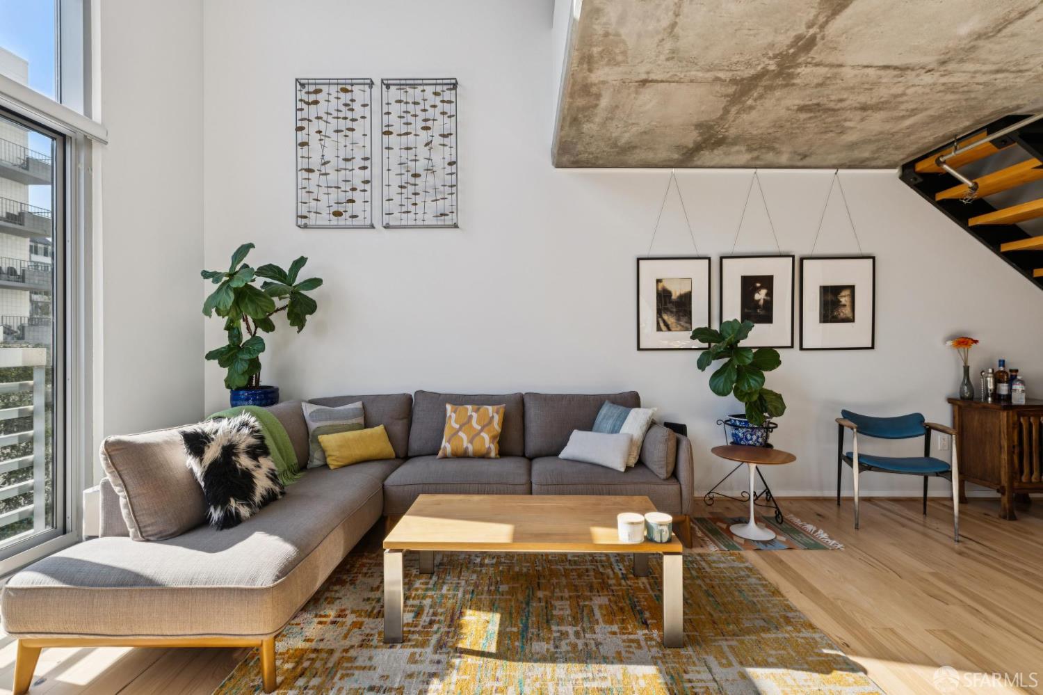 Living room with a gray sectional sofa, large windows, and an exposed concrete ceiling.