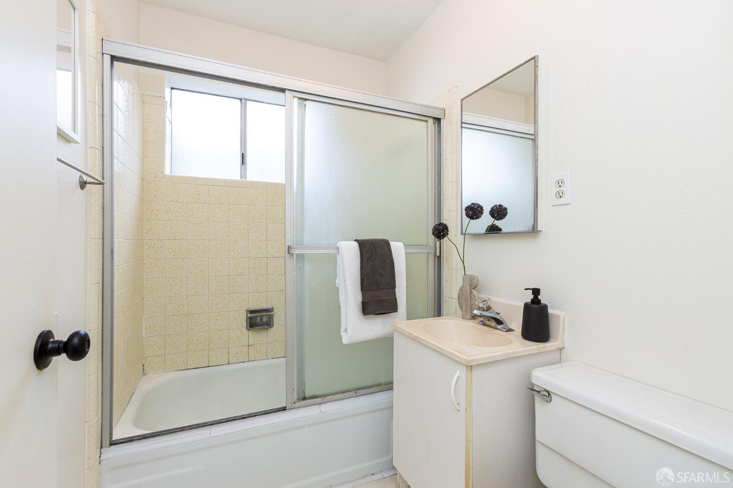 Bathroom with a tub-shower behind frosted sliding doors, a compact sink vanity, mirror, and toilet.