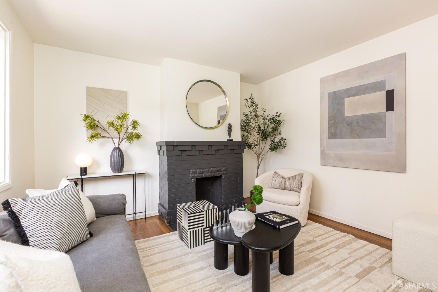 Staged living room with a dark brick fireplace, gray sofa, cream armchair, and striped rug.