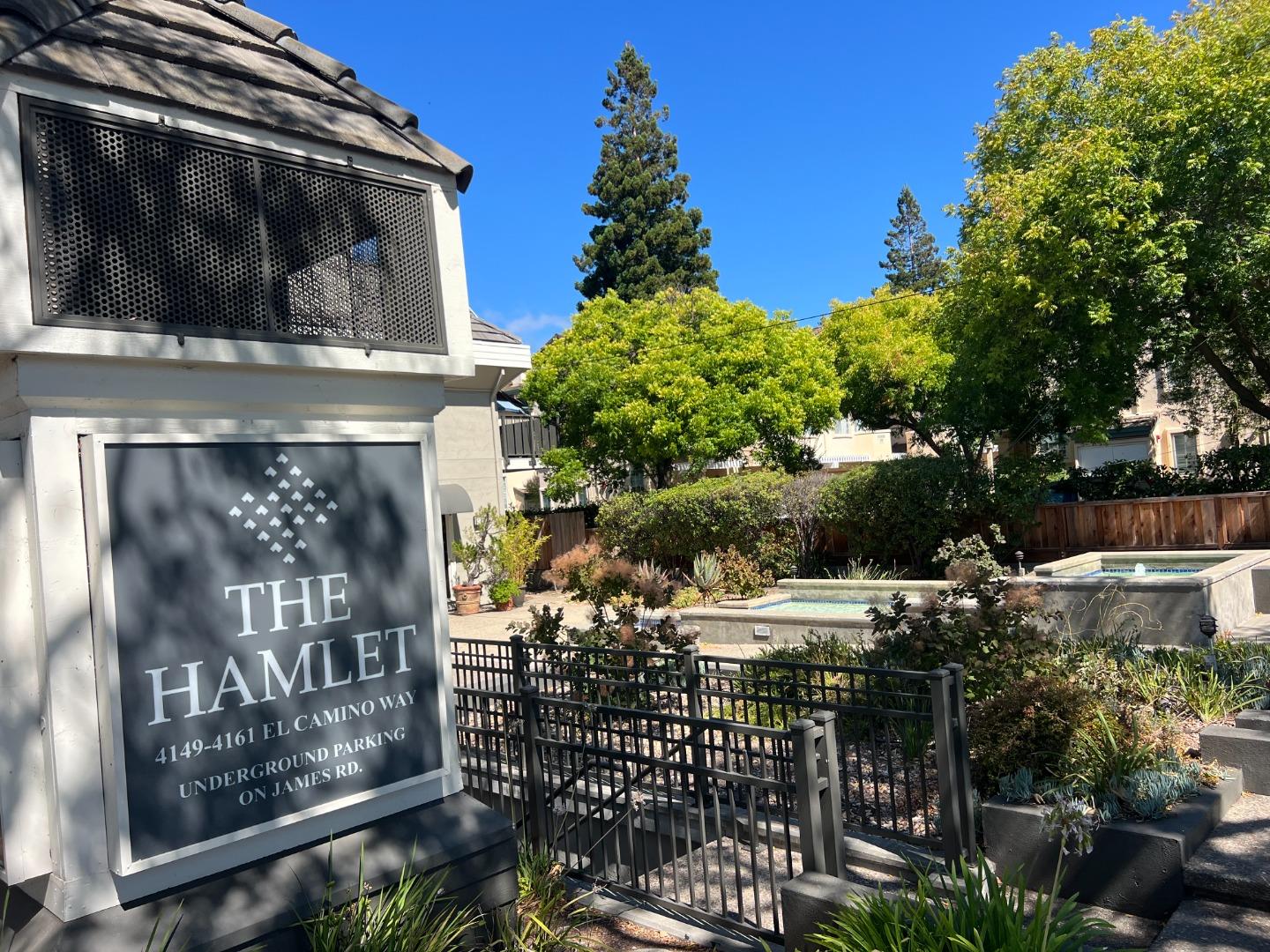 The Hamlet community entrance sign beside a landscaped courtyard with two pools or spas.