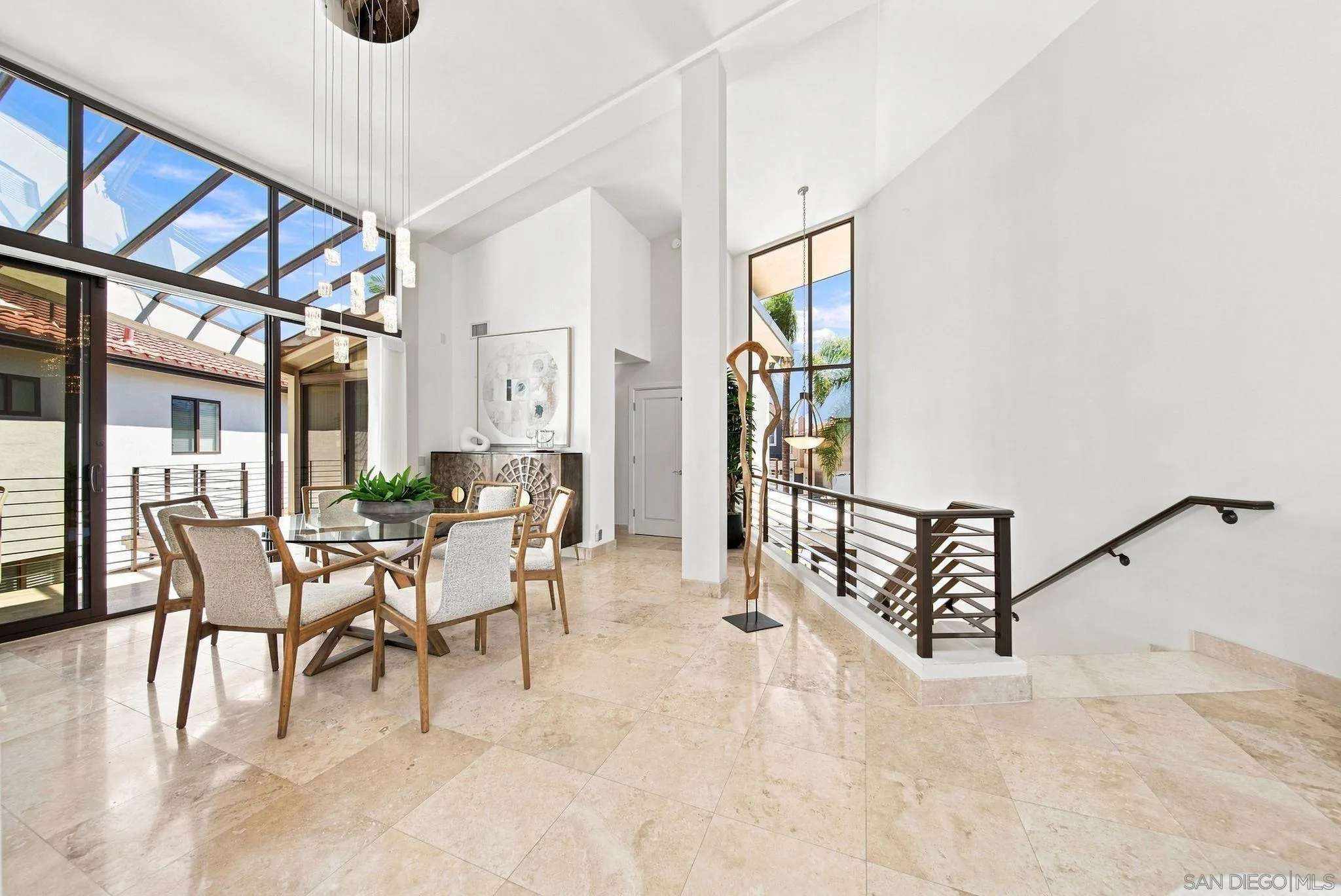 Dining area with a glass table beneath tall windows and a dramatic high ceiling.