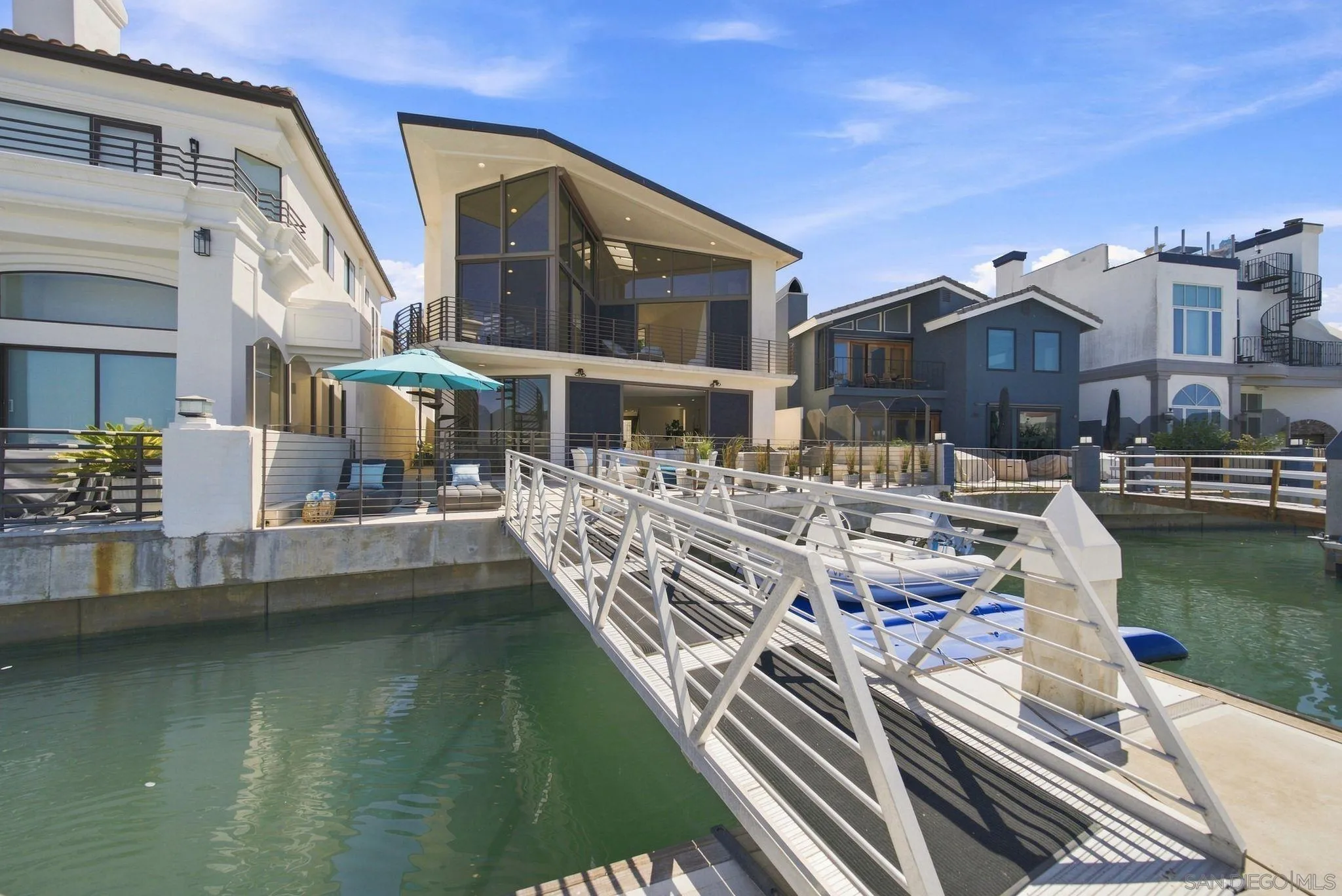 Modern canal-front home with glass walls, a white gangway, and a boat docked alongside.