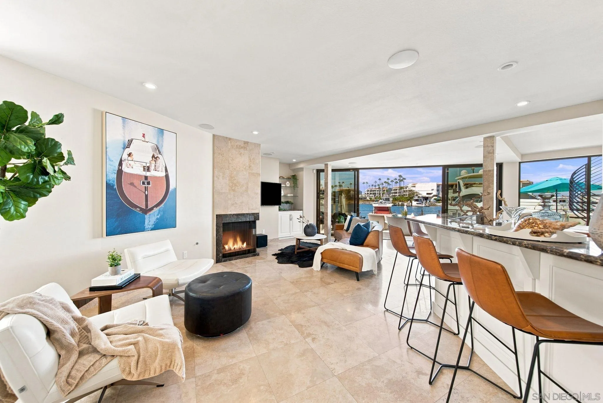 Living room with fireplace and kitchen bar overlooking a marina through floor-to-ceiling windows.