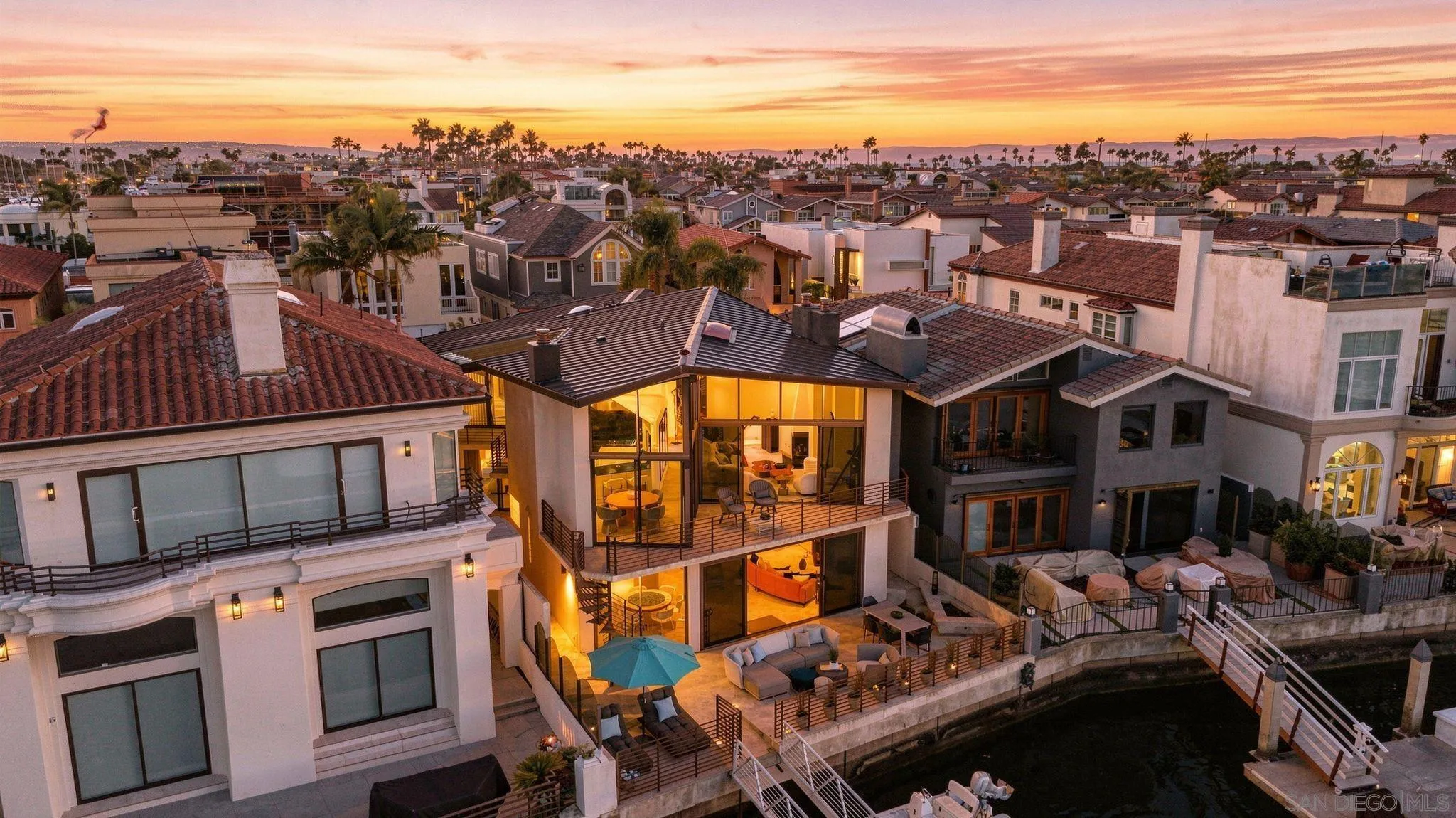 Aerial view of a glass-fronted waterfront home and canal-side terrace at sunset.