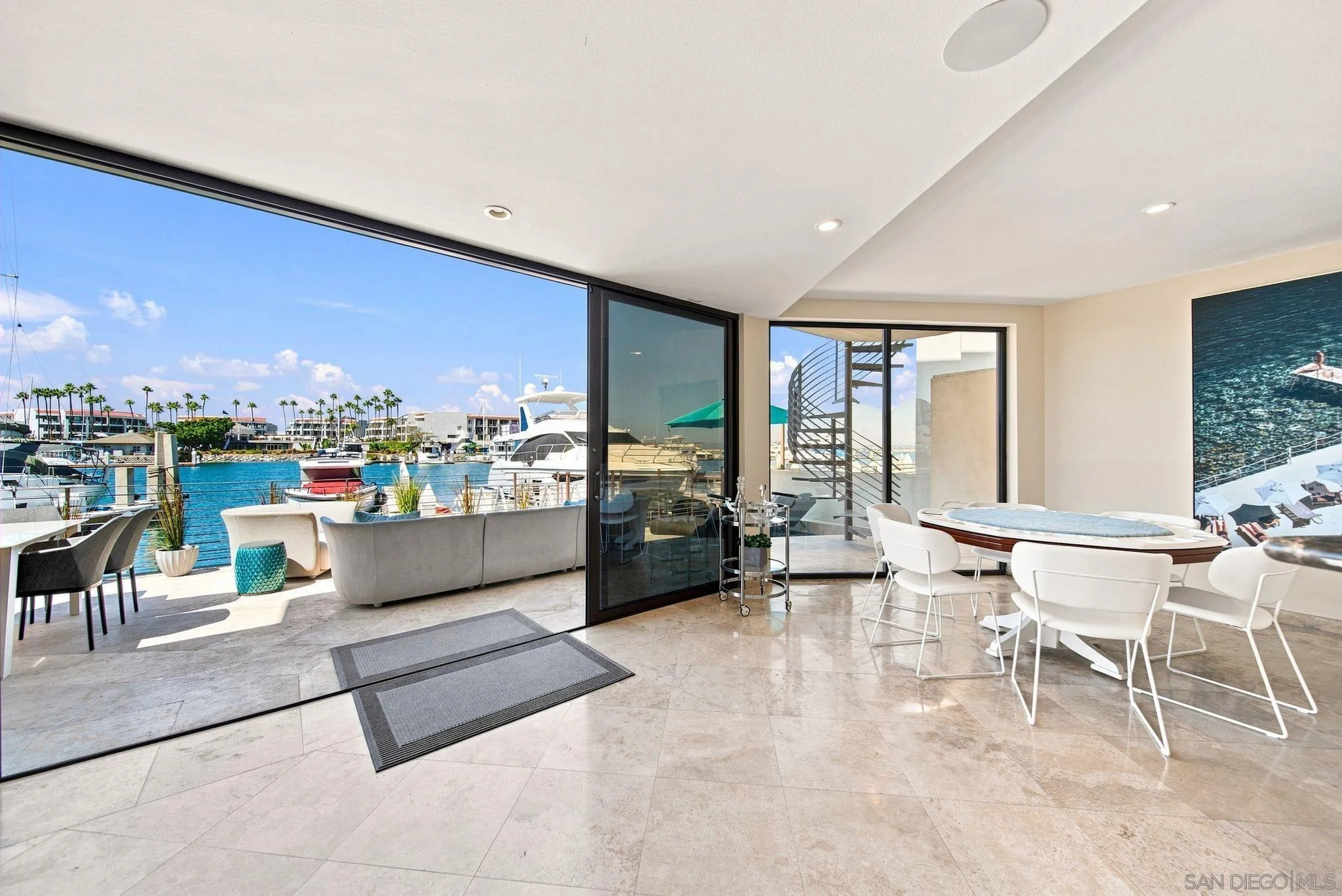 Furnished living and dining area opens onto a patio overlooking a marina with boats and blue water.