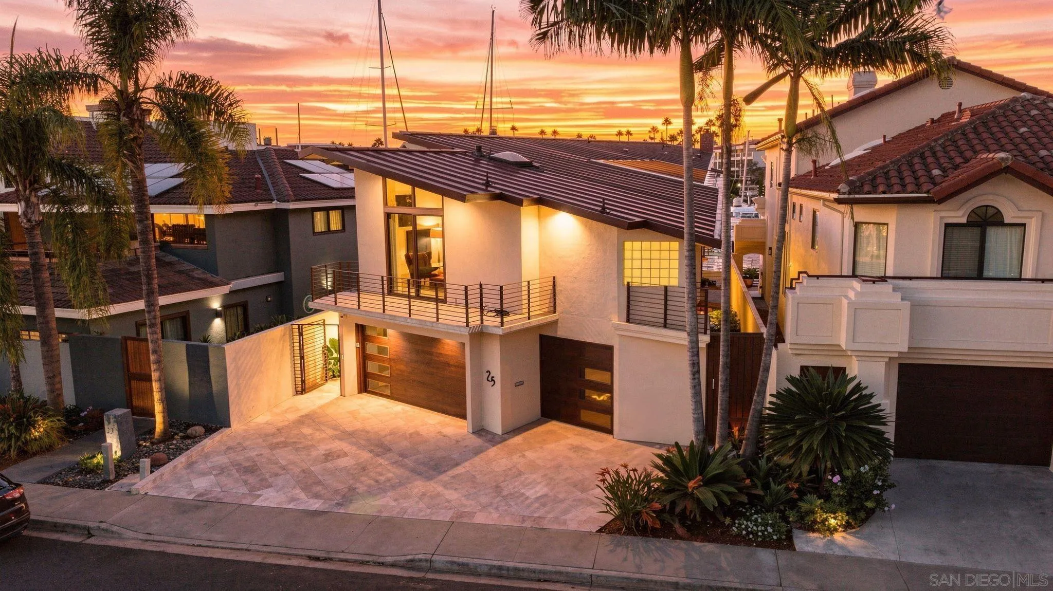 Modern two-story home with a balcony and wood garage doors beneath a vivid sunset sky.