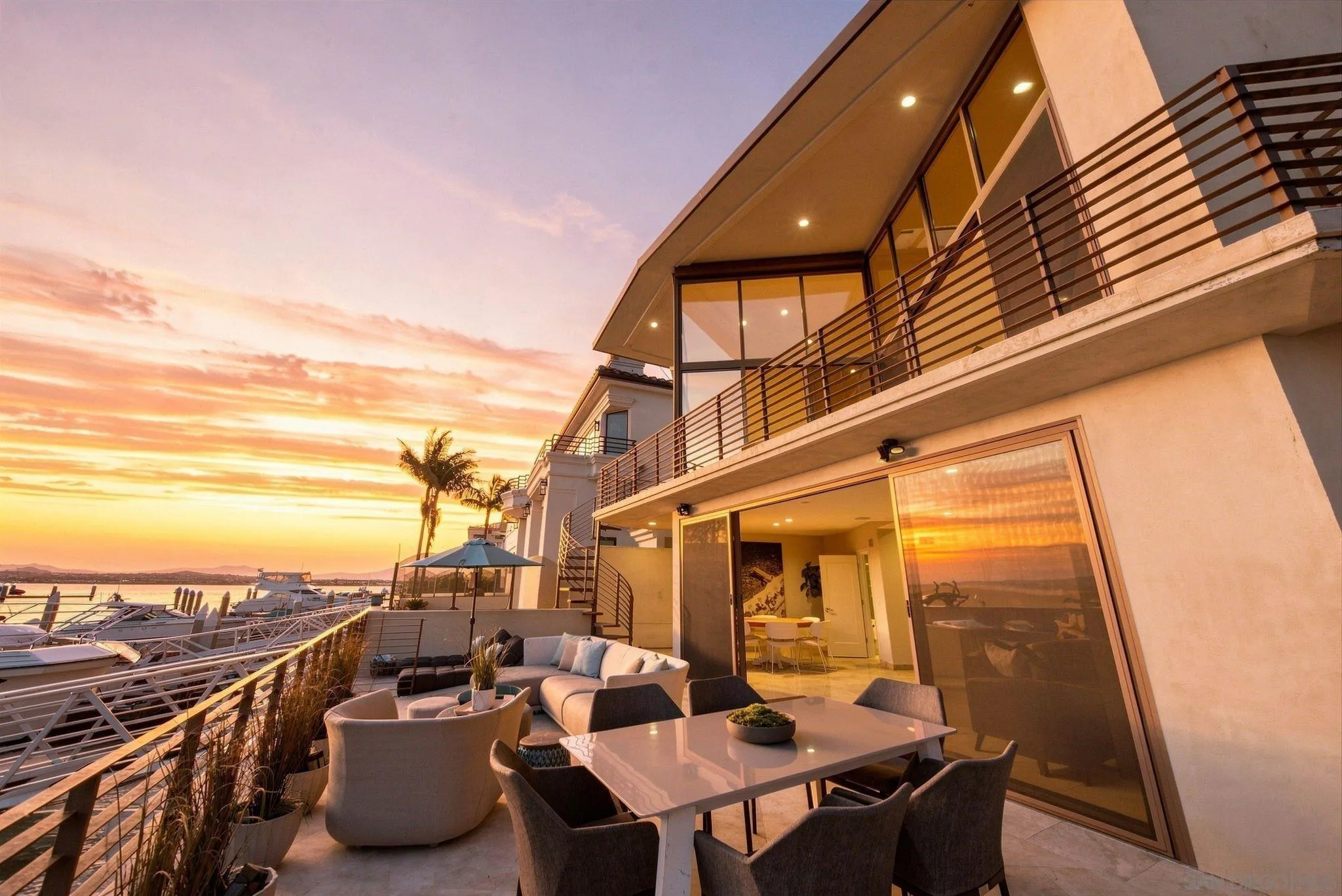 Waterfront terrace with outdoor dining and lounge seating overlooking a marina at sunset.