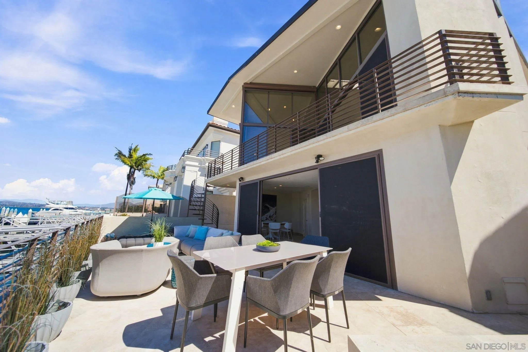 Waterfront patio with outdoor dining and lounge seating beside a modern home and marina.