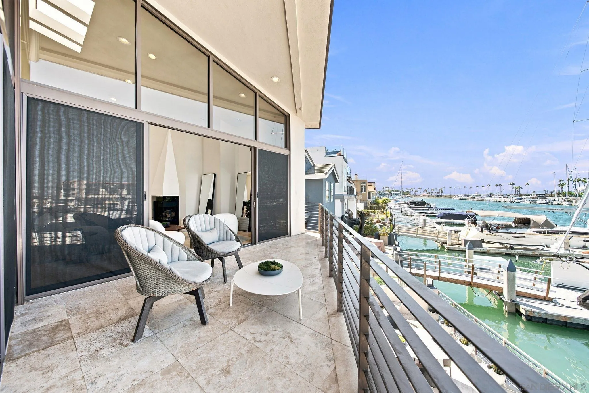 Furnished tiled balcony overlooking a marina, with wicker chairs and boats moored alongside.