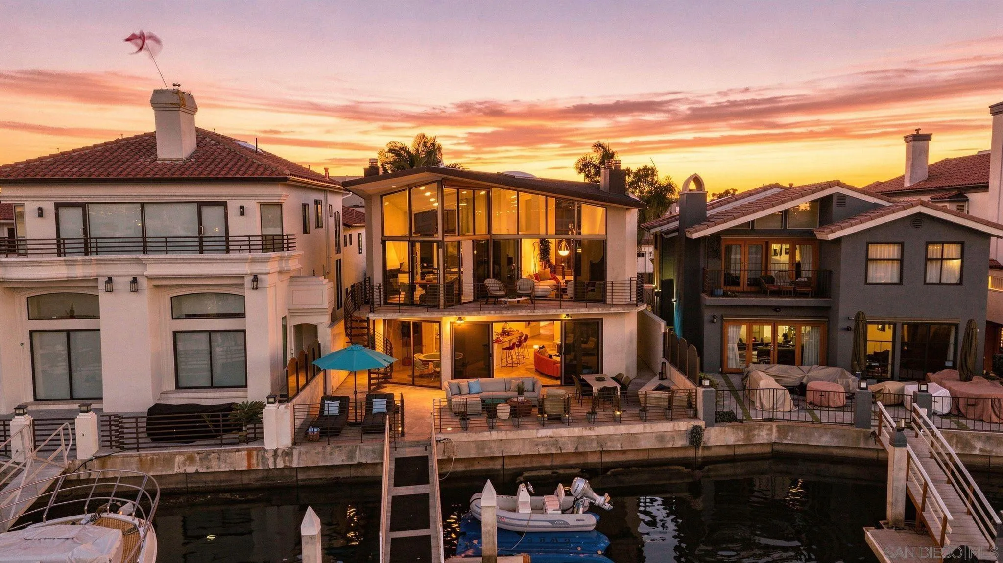 Waterfront home with a glass façade and furnished terraces beside a canal at sunset.