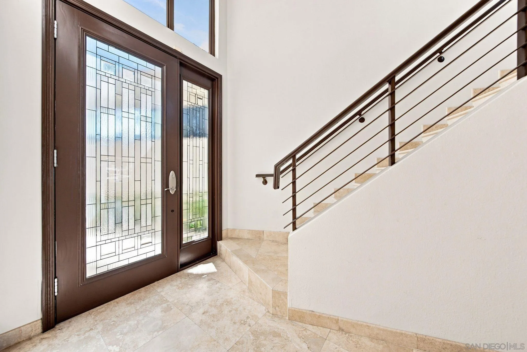 Entry foyer with geometric leaded-glass front door, stone tile floor, and staircase with dark metal railing.