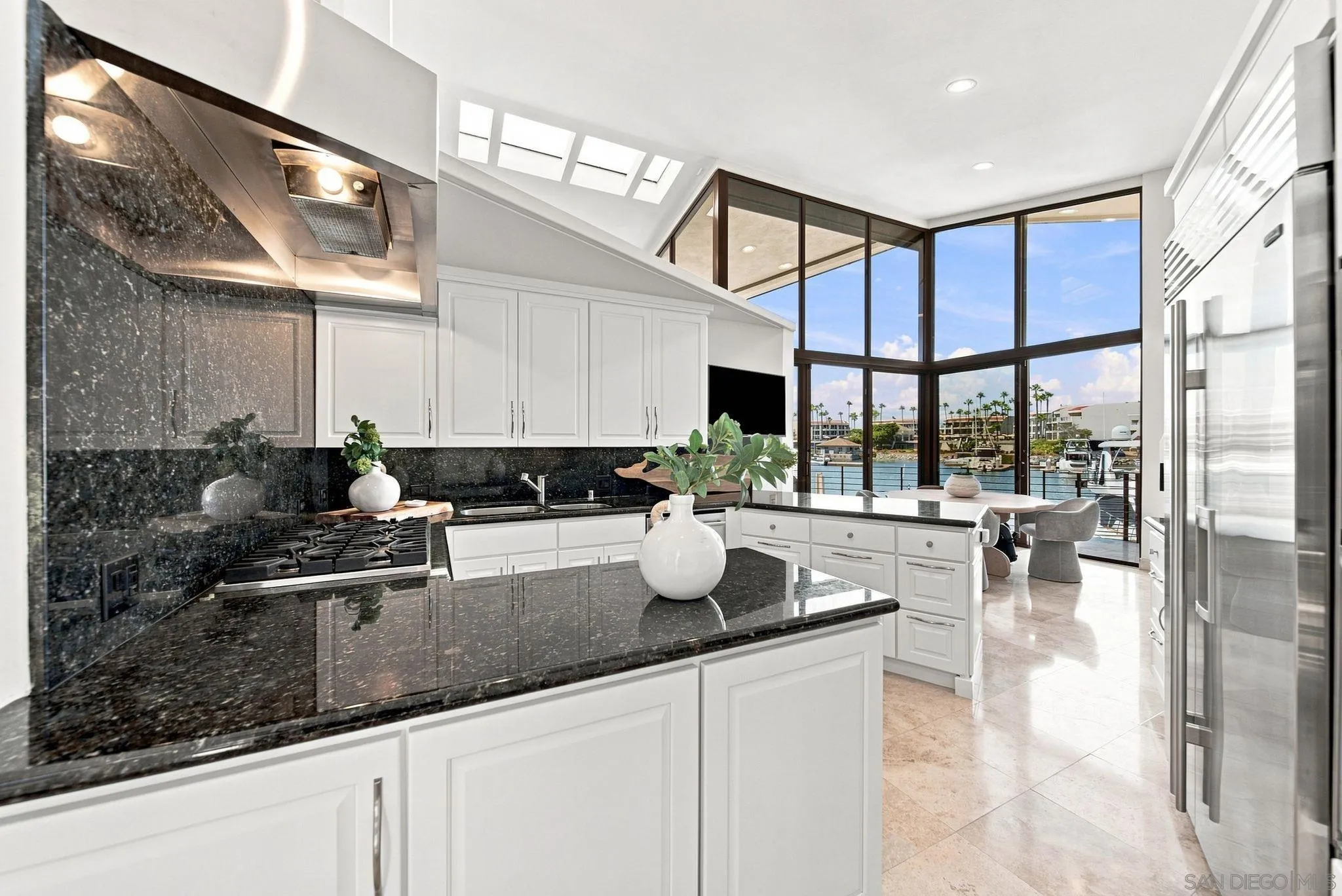 Waterfront kitchen with black stone counters, white cabinetry, and floor-to-ceiling marina views.