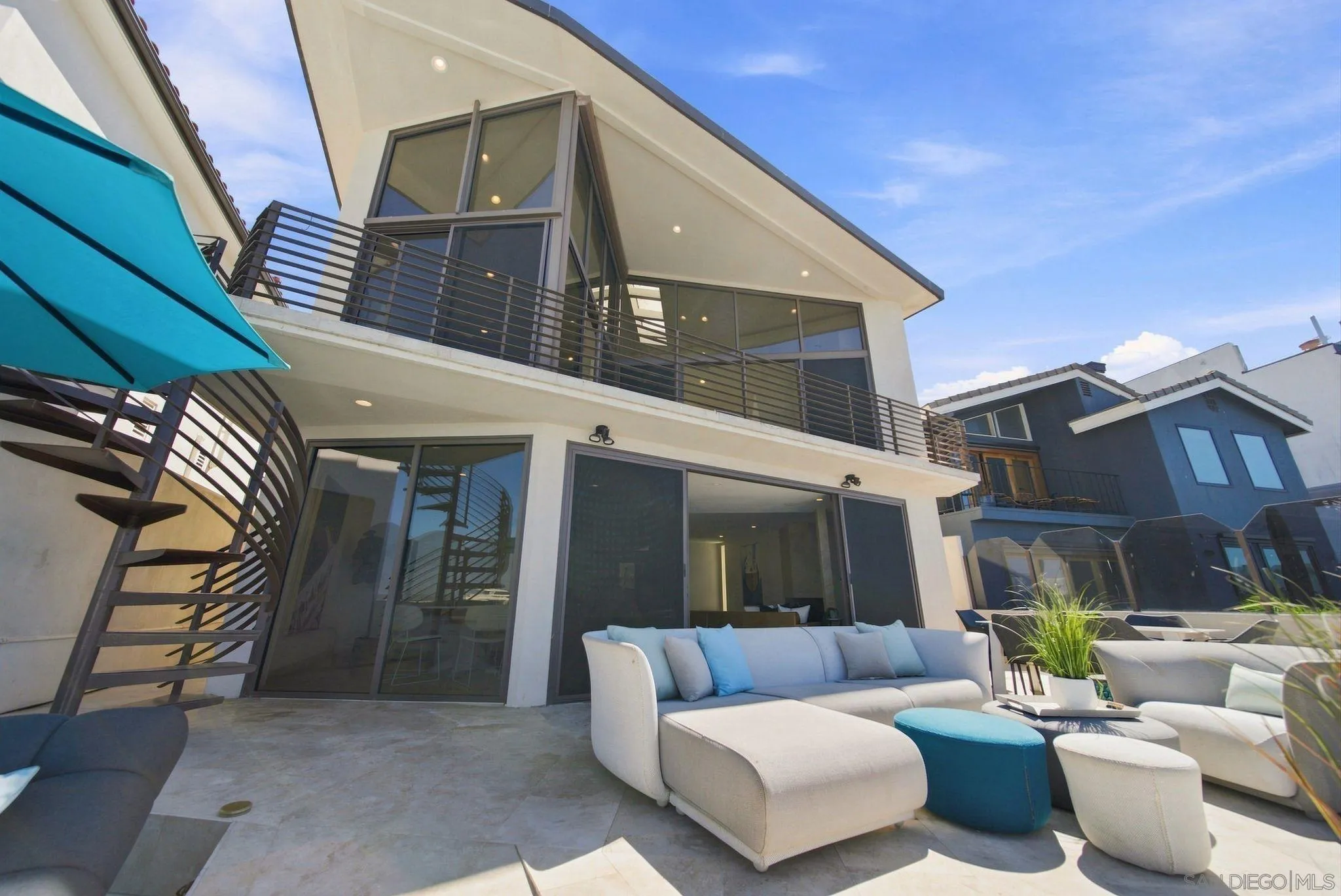 Modern coastal home with a furnished patio, spiral staircase, and bright blue umbrella.