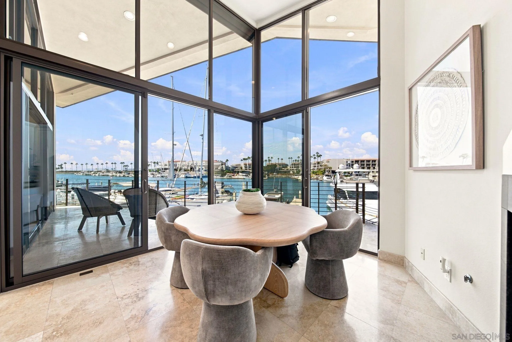 Dining area with floor-to-ceiling marina views, a sculptural wood table, and upholstered chairs.