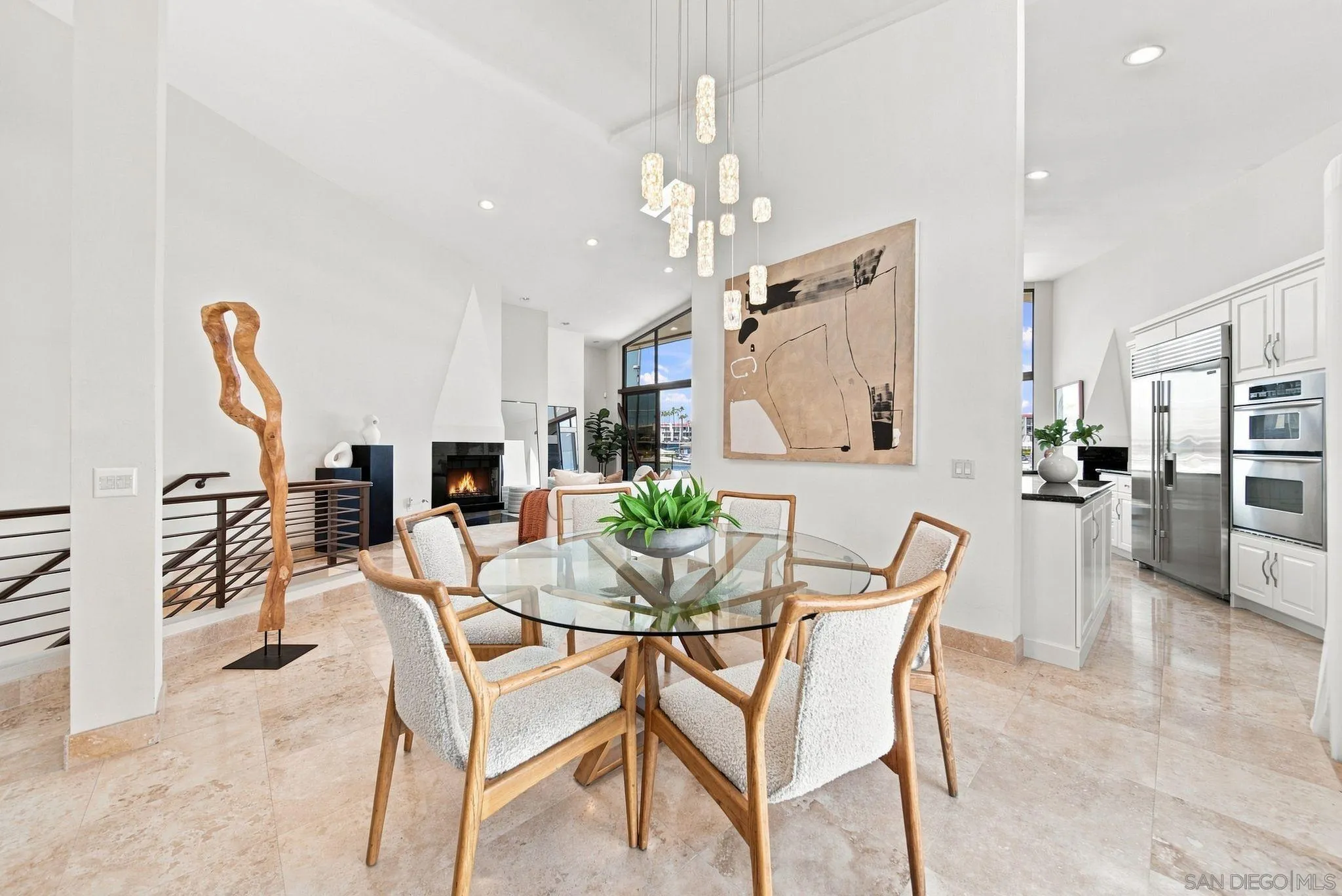 Dining area with a round glass table, pendant lights, and an adjoining kitchen and fireplace.