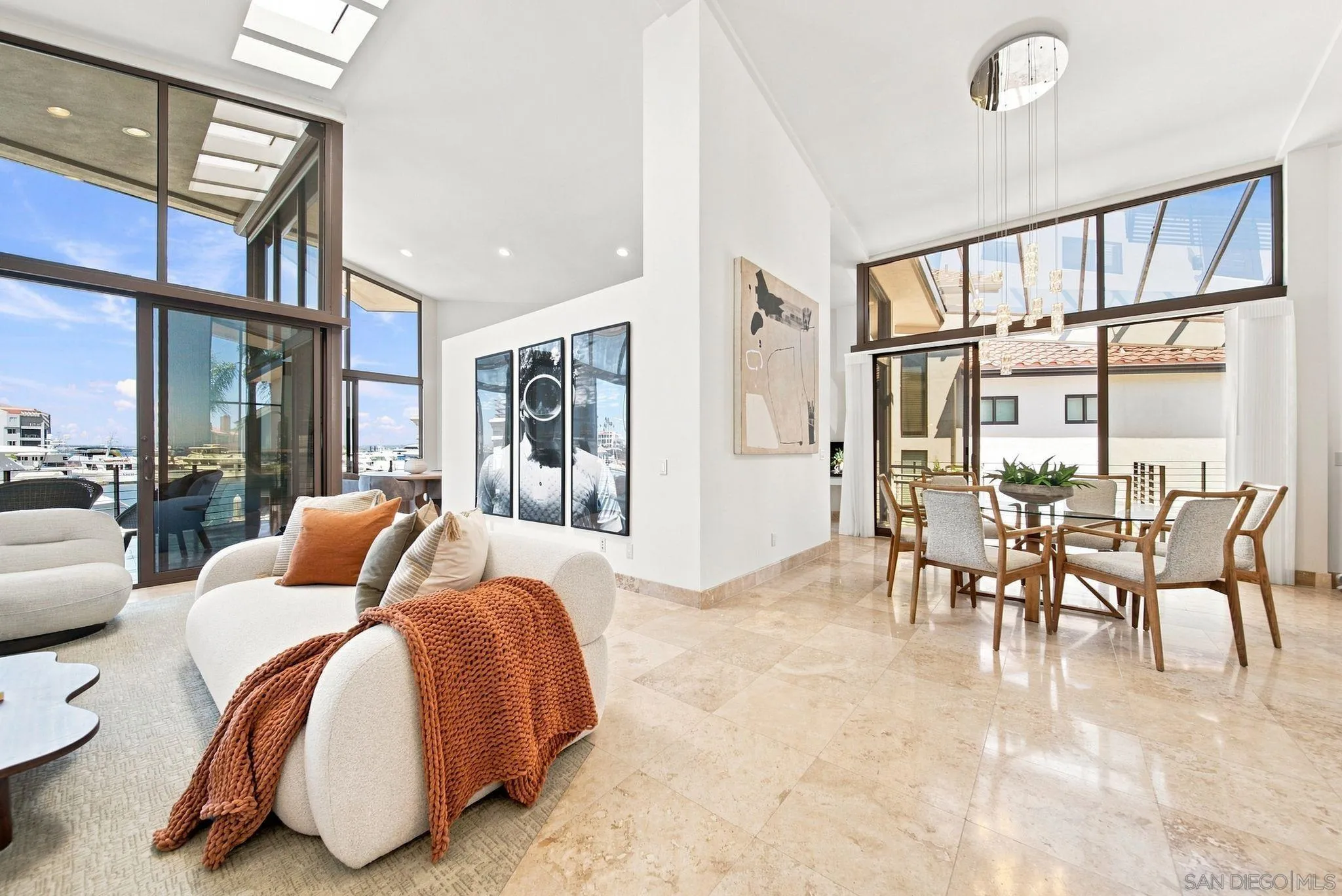 Open-plan living and dining room with tall marina-facing windows and cream seating.