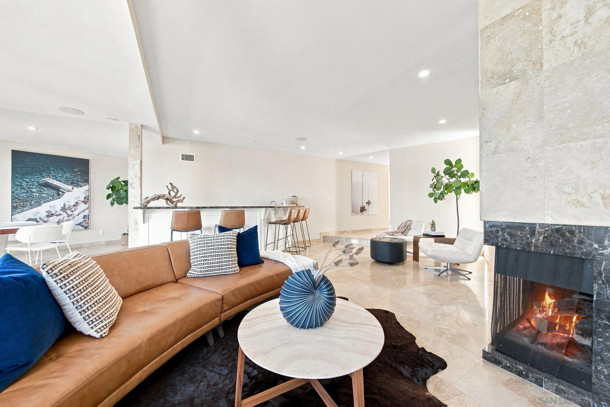 Staged living room with a tan sectional, blue accents, bar seating, and a lit stone fireplace.