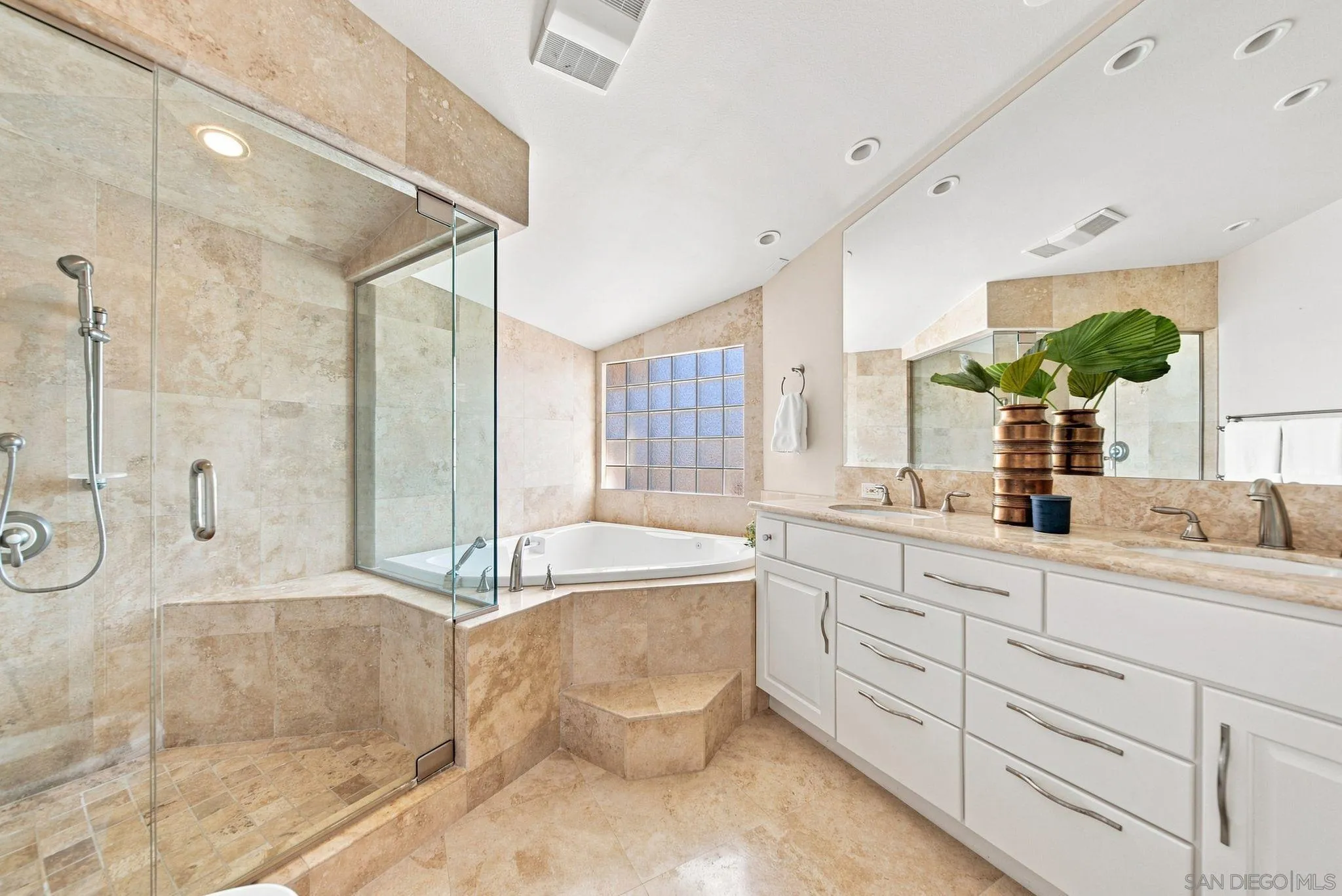 Primary bathroom with a glass shower, corner soaking tub, and long double vanity.