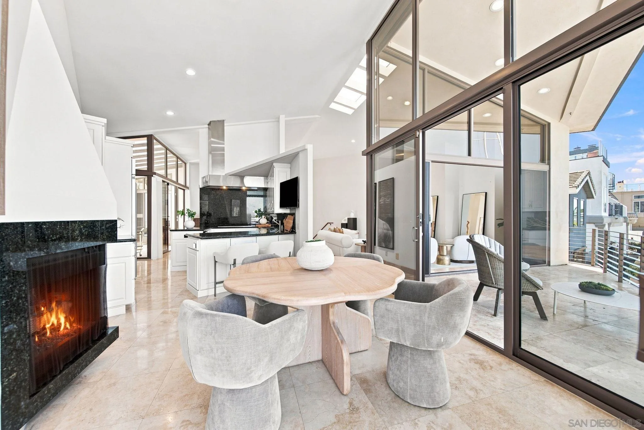 Open-plan dining area with a round table, black stone fireplace, and glass doors to a balcony.