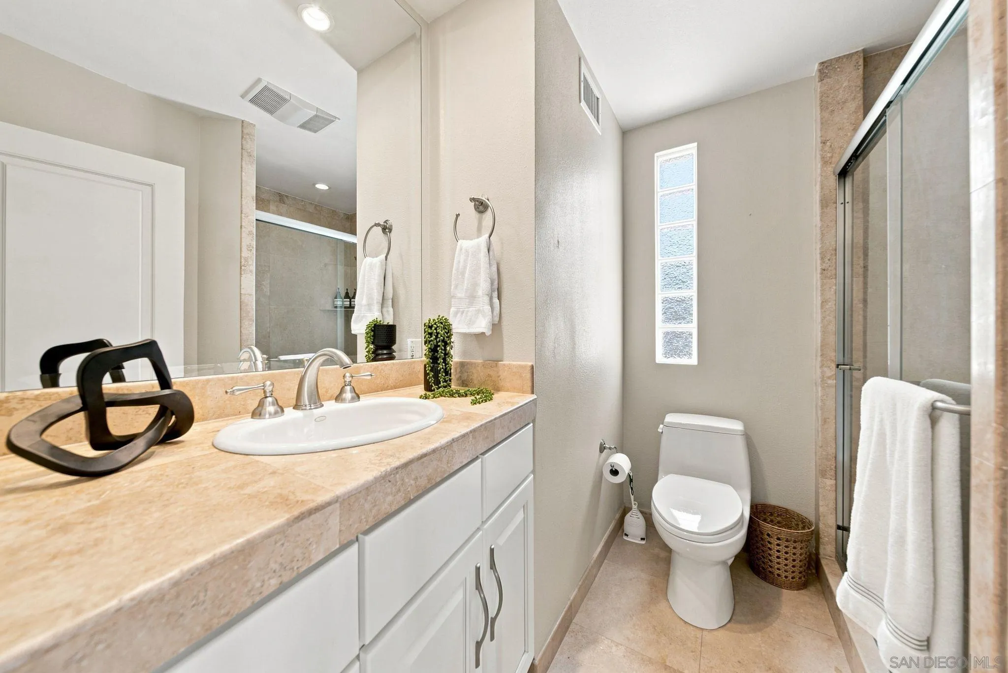 Bathroom with a beige stone vanity, large mirror, toilet, and glass-enclosed shower.
