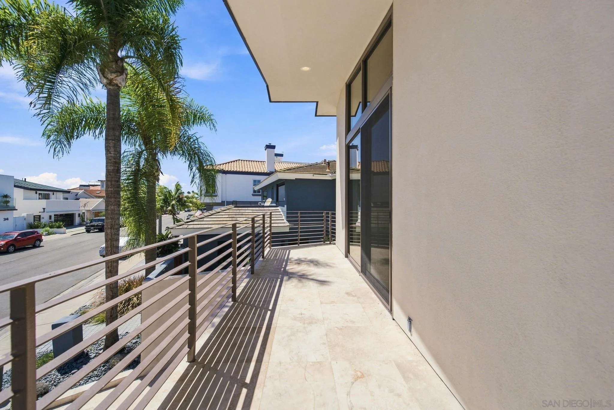 Tiled balcony with metal railing overlooking palm trees and neighboring homes.