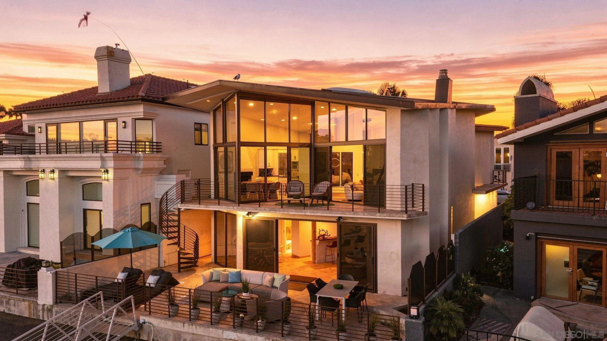 Multi-level home with glass walls and furnished terraces glowing at sunset.