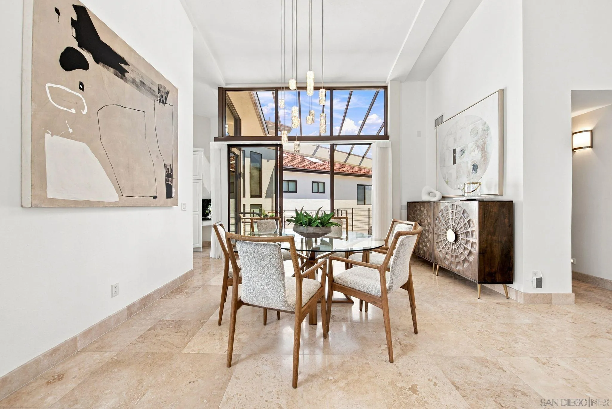 Dining room with a round glass table, pendant lights, and a glass ceiling above large windows.