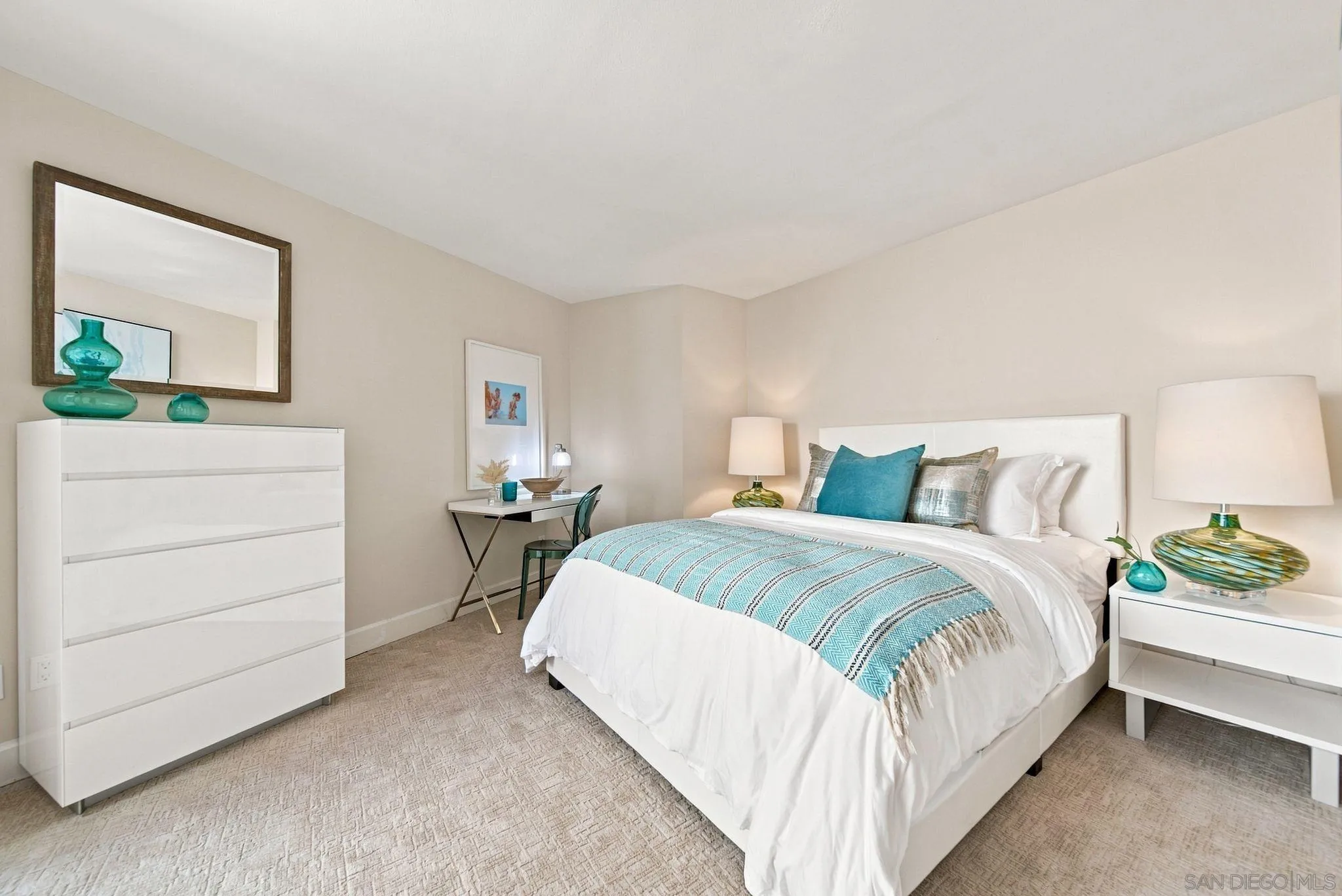 Staged bedroom with a white bed and turquoise throw, teal accents, and white furniture.