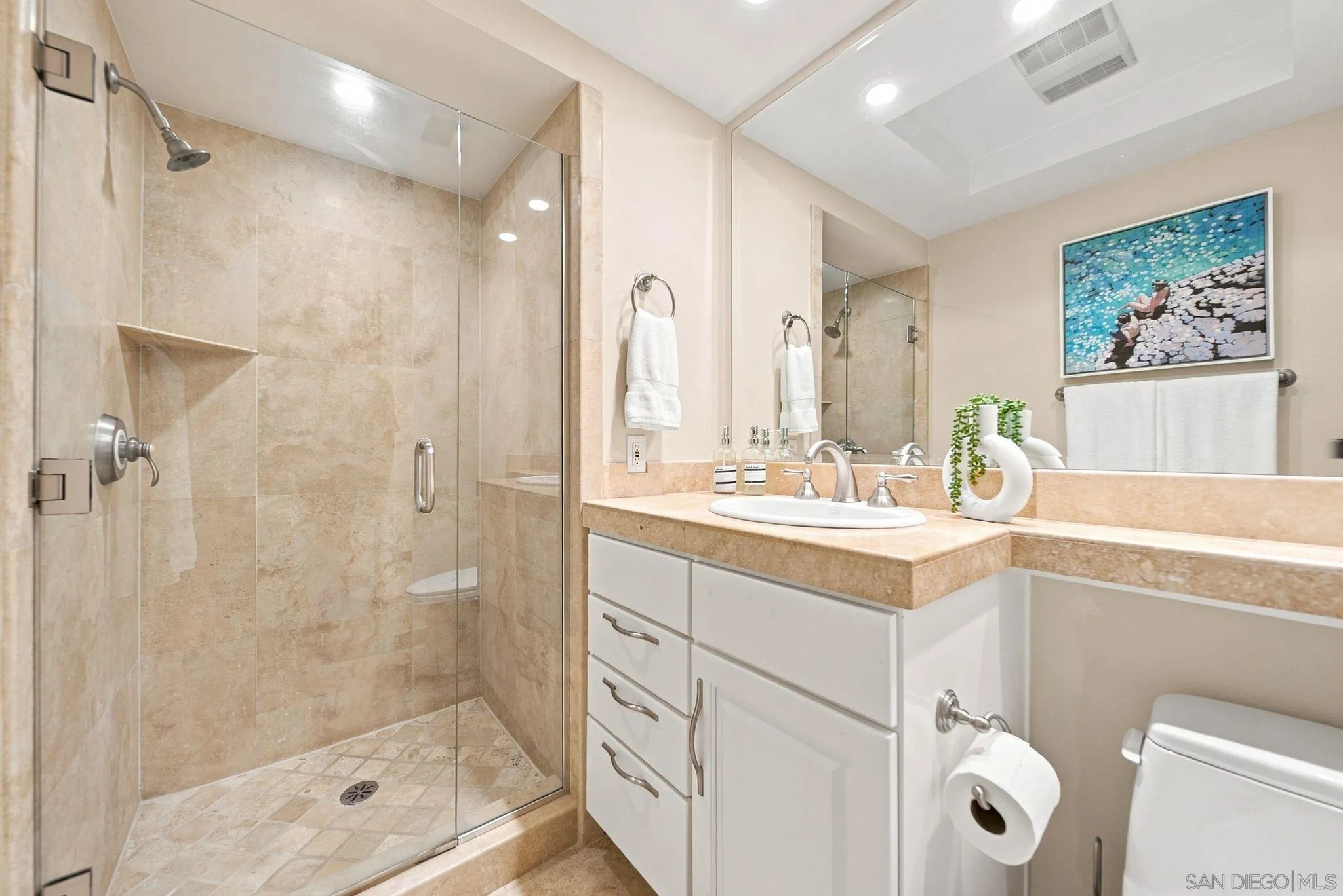 Bathroom with a glass-enclosed beige stone shower and white vanity.