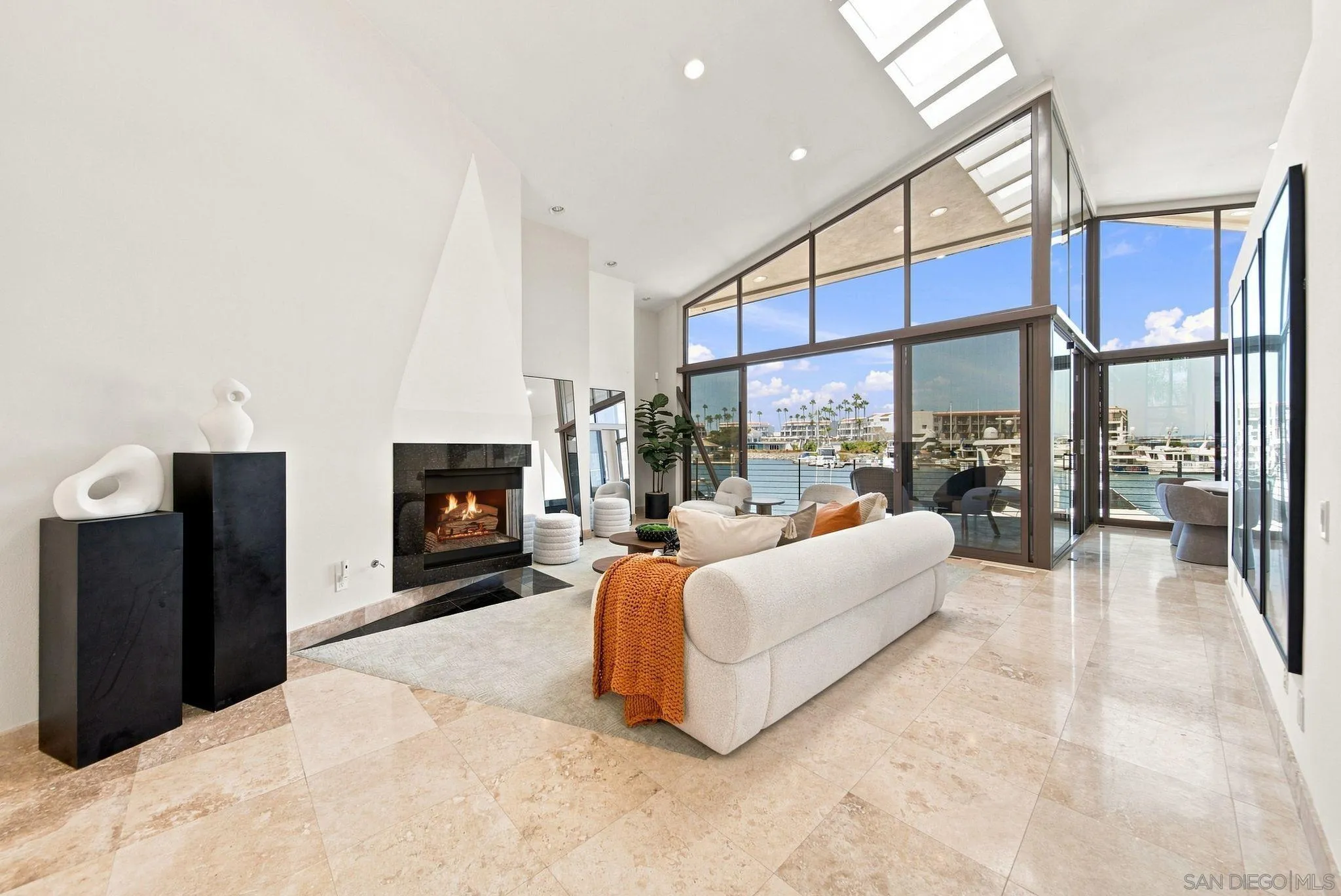 Staged living room with a fireplace and expansive glass walls overlooking a marina.