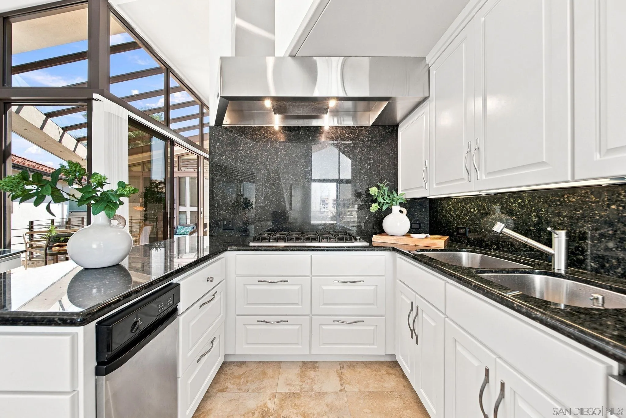 Kitchen with white cabinets, black stone counters, and tall slanted windows overlooking a patio.