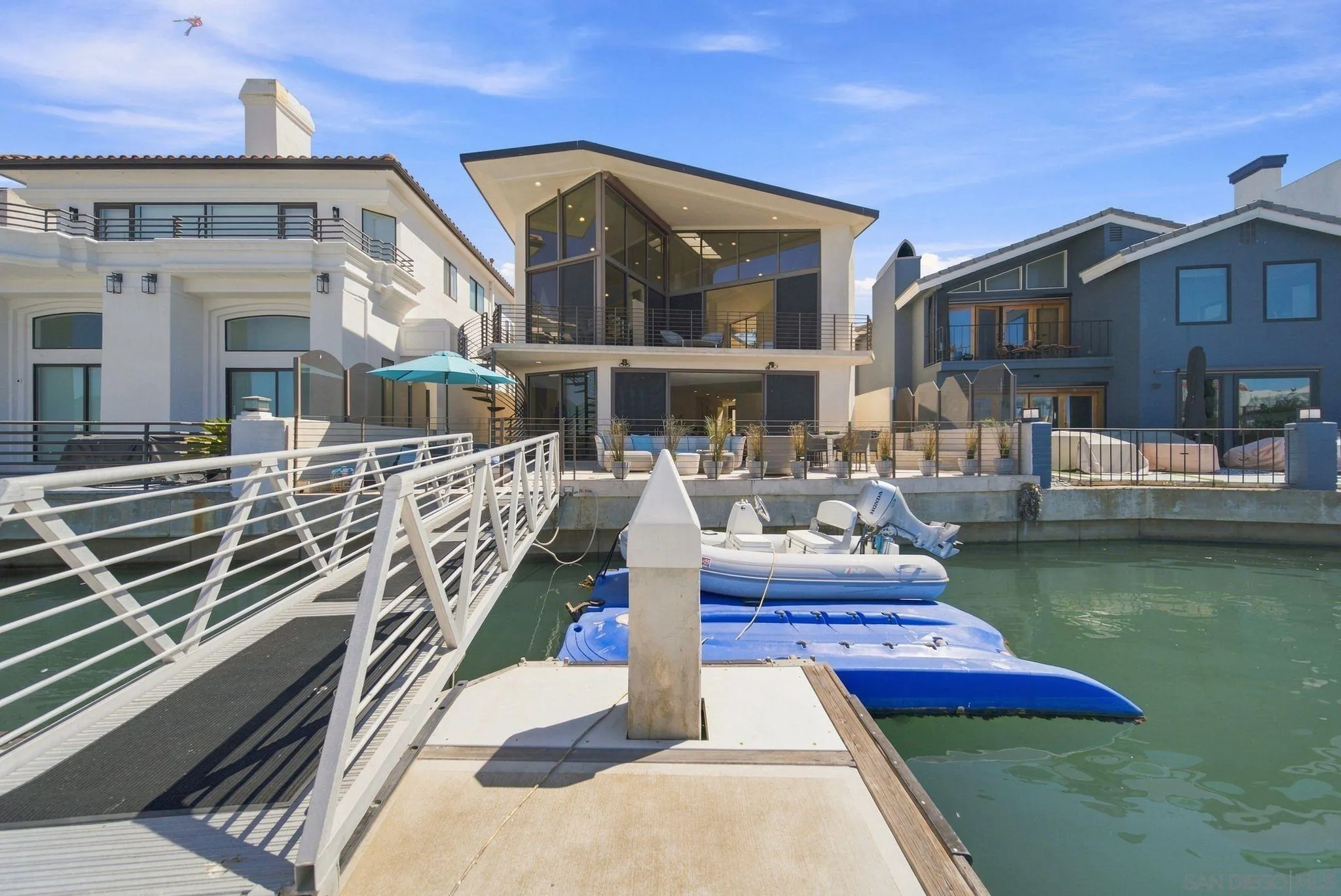 Modern waterfront home with glass walls, a dock gangway, and boats moored in front.